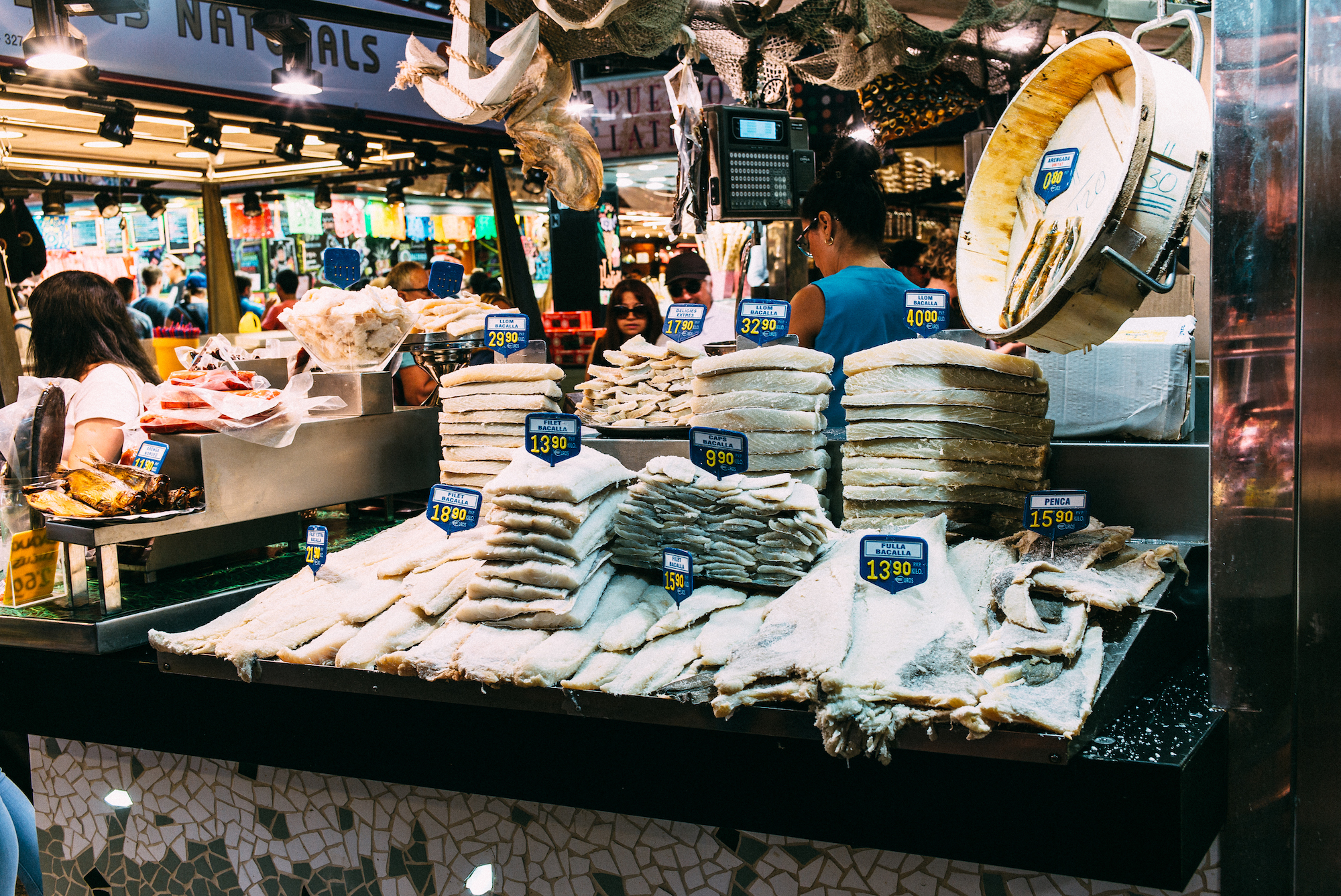 Stacks of salted cod fillets with price tags at a fish stall inside Mercat de la Boqueria in Barcelona.