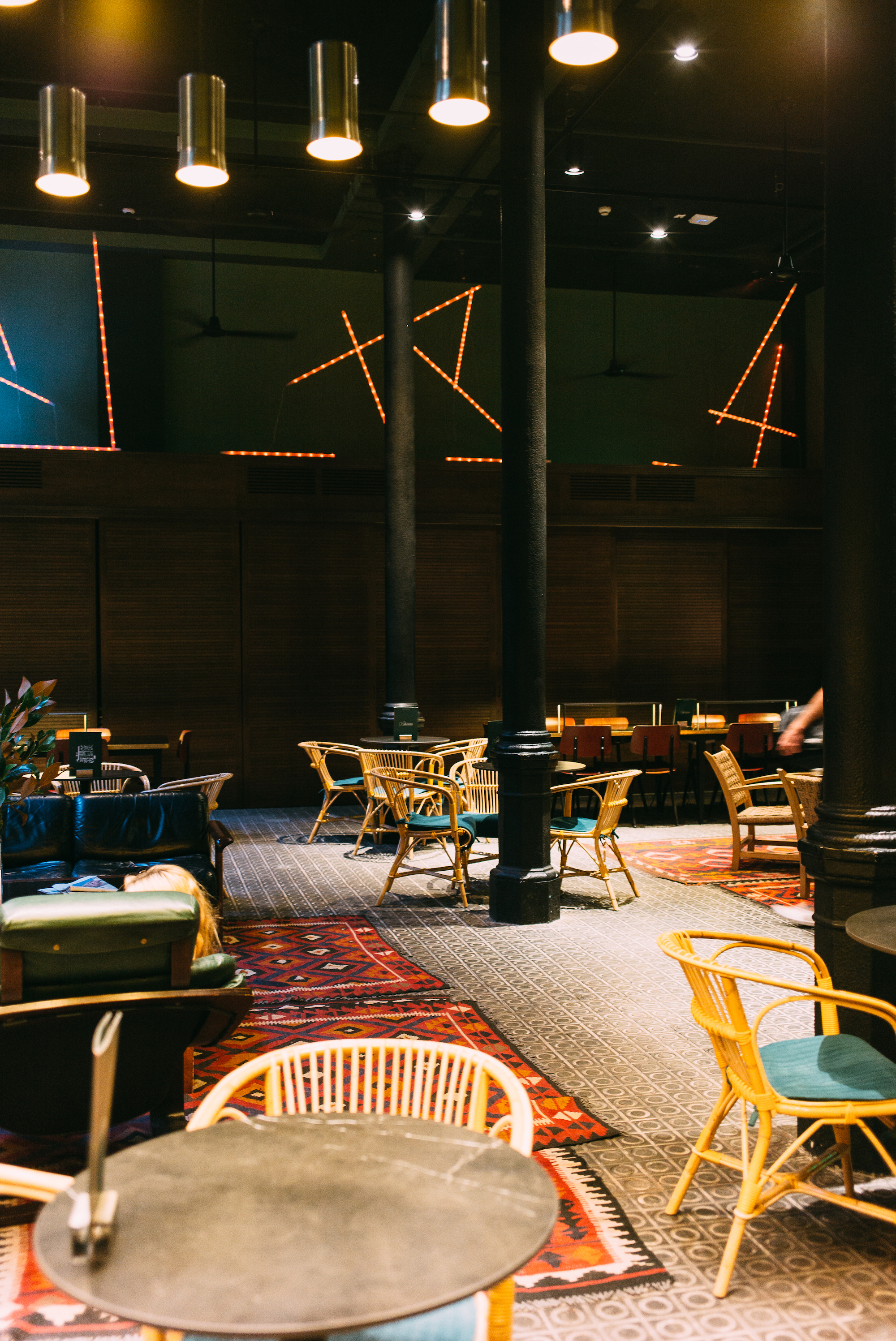 Hotel lounge with yellow wicker chairs, patterned tiles, vintage rugs, and hanging lamps in Barcelona.