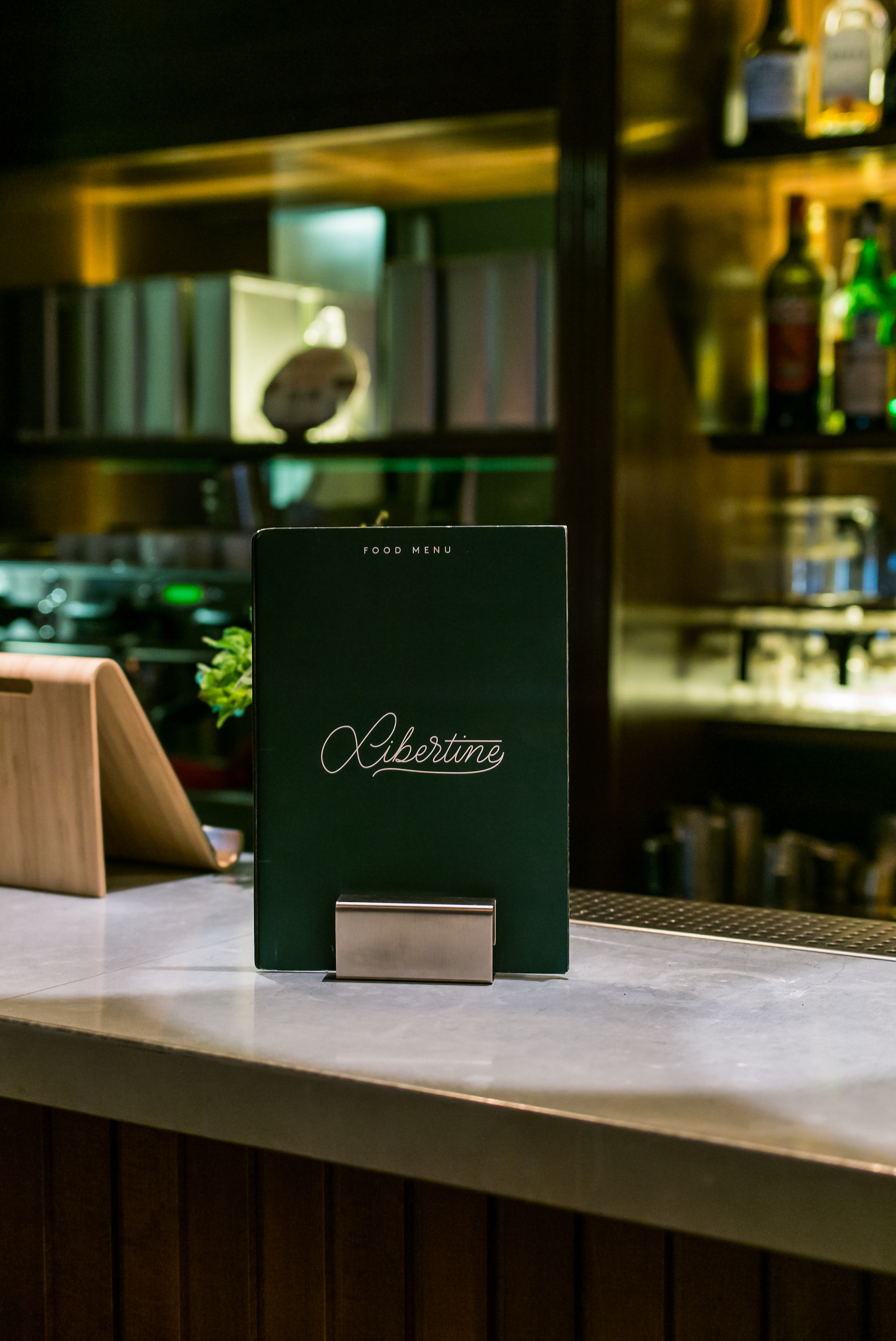 Forest green 'Libertine' food menu card resting in a stainless stand on a bar counter at Casa Bonay, Barcelona.
