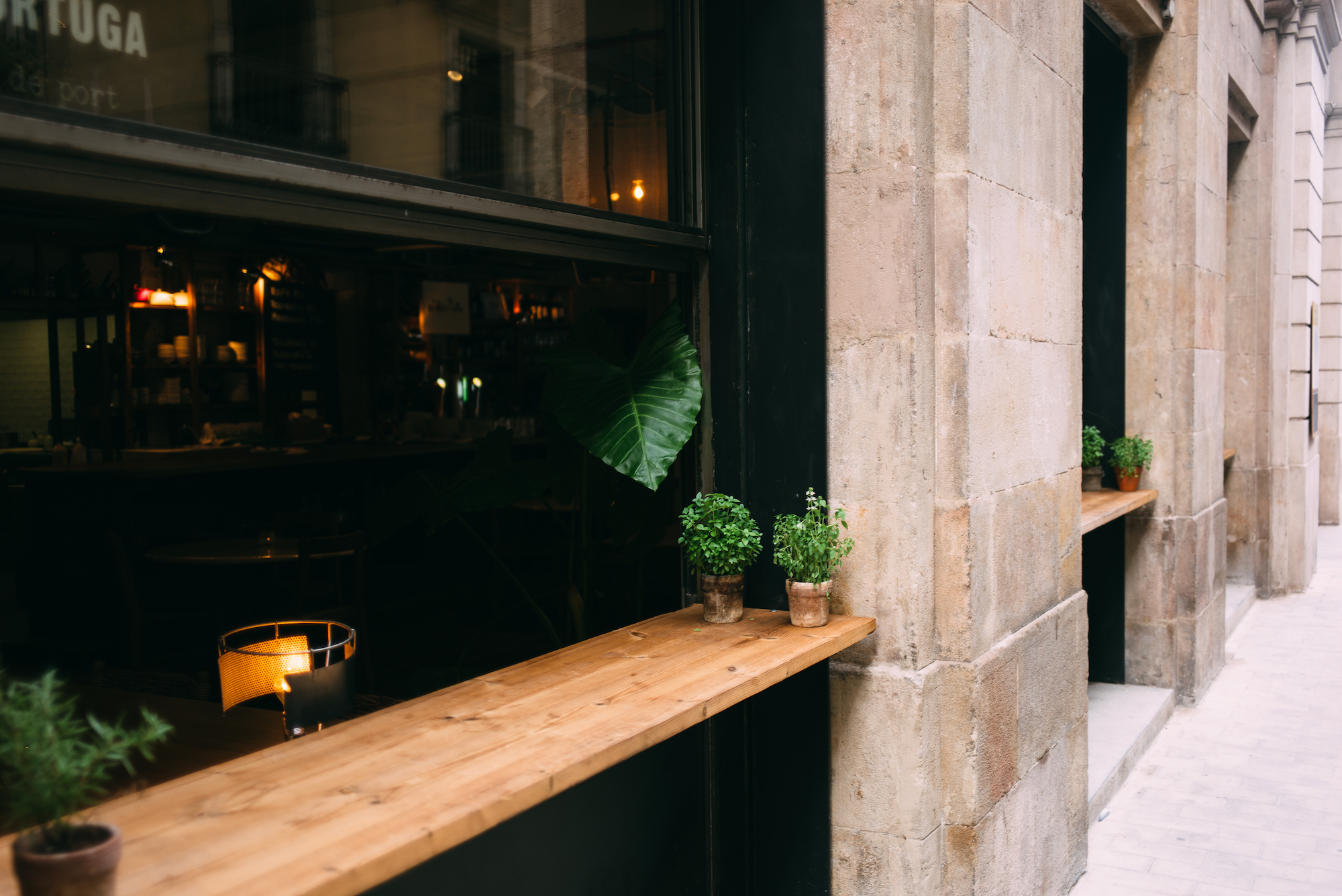 Small potted basil and herbs resting on a wooden window counter ledge of an open cafe along a stone street in Barcelona, shot with a Leica M240.