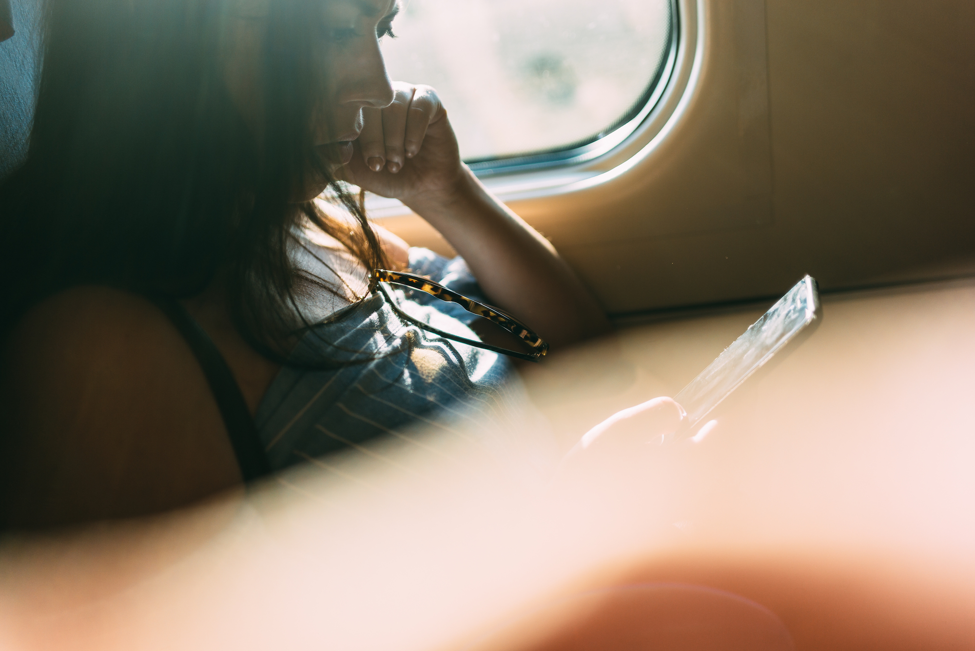 Woman seated inside a sunlit passenger train gazing at her smartphone with warm sunlight illuminating her.