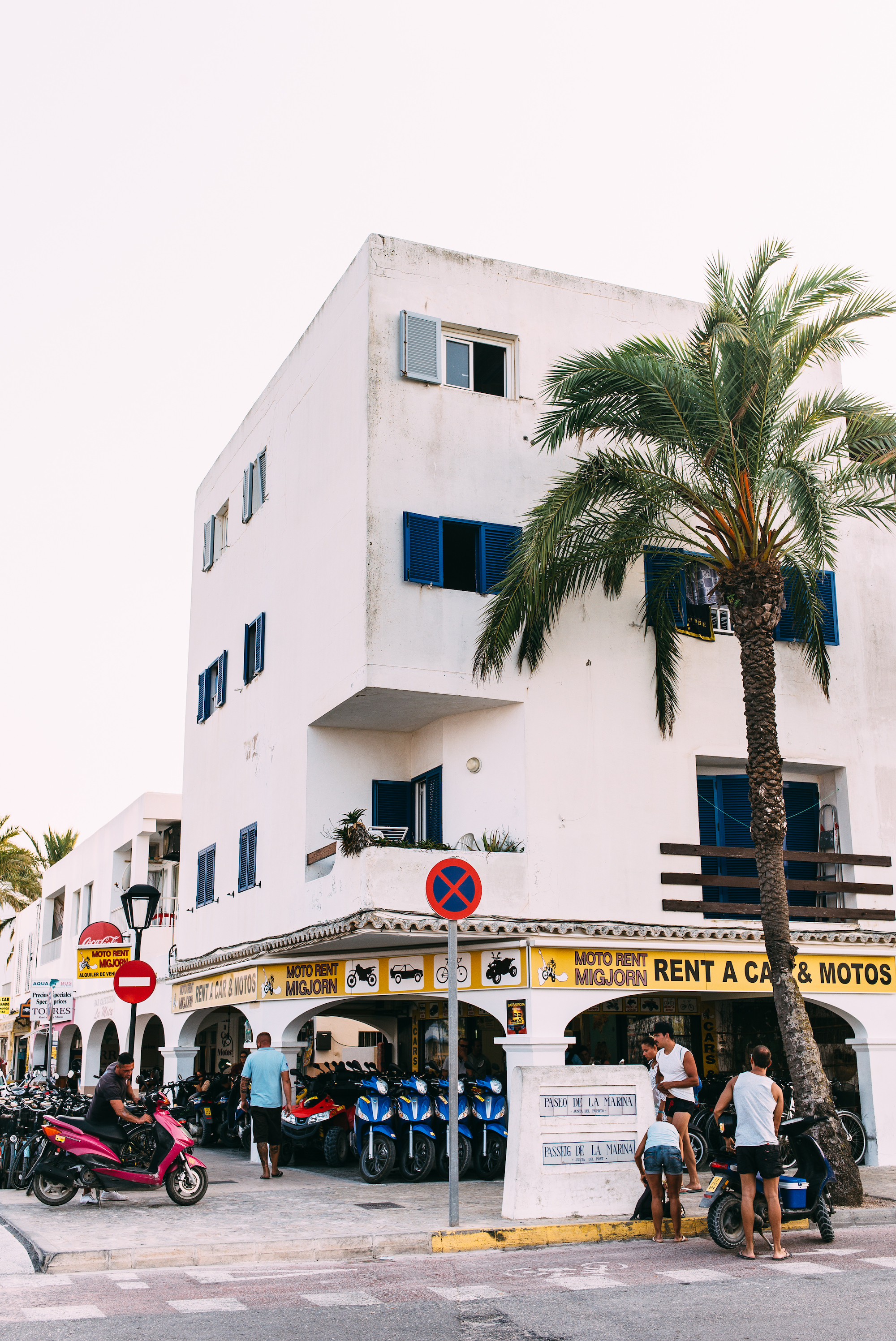 White stucco building with blue shutters above the 'Moto Rent Migjorn' shop in La Savina, Formentera.