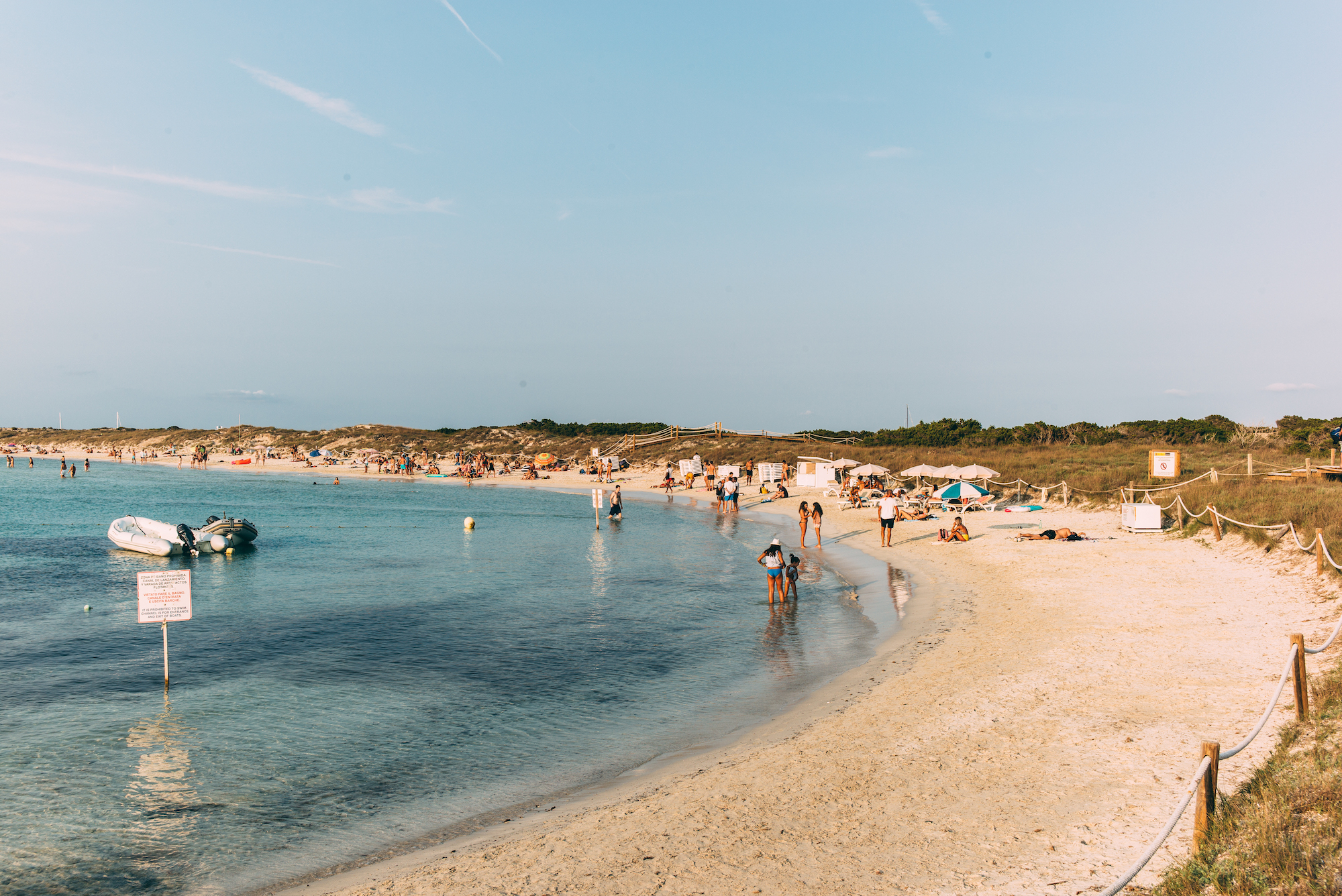 Curving sandy beach cove with umbrellas, sunbathers, and an inflatable dinghy boat in Formentera.