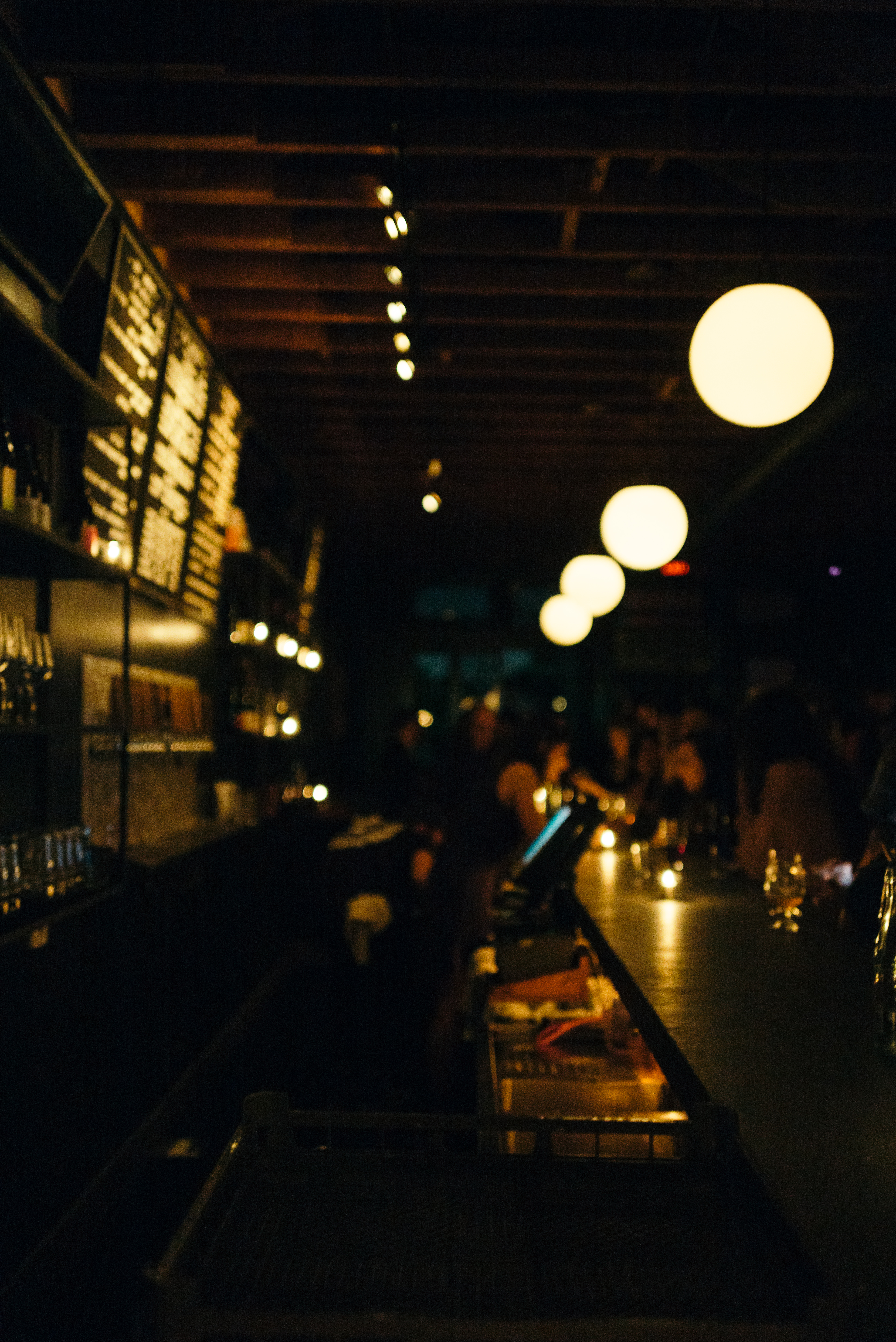 Moody bar interior with glowing spherical pendant lights illuminating patrons seated along the counter.
