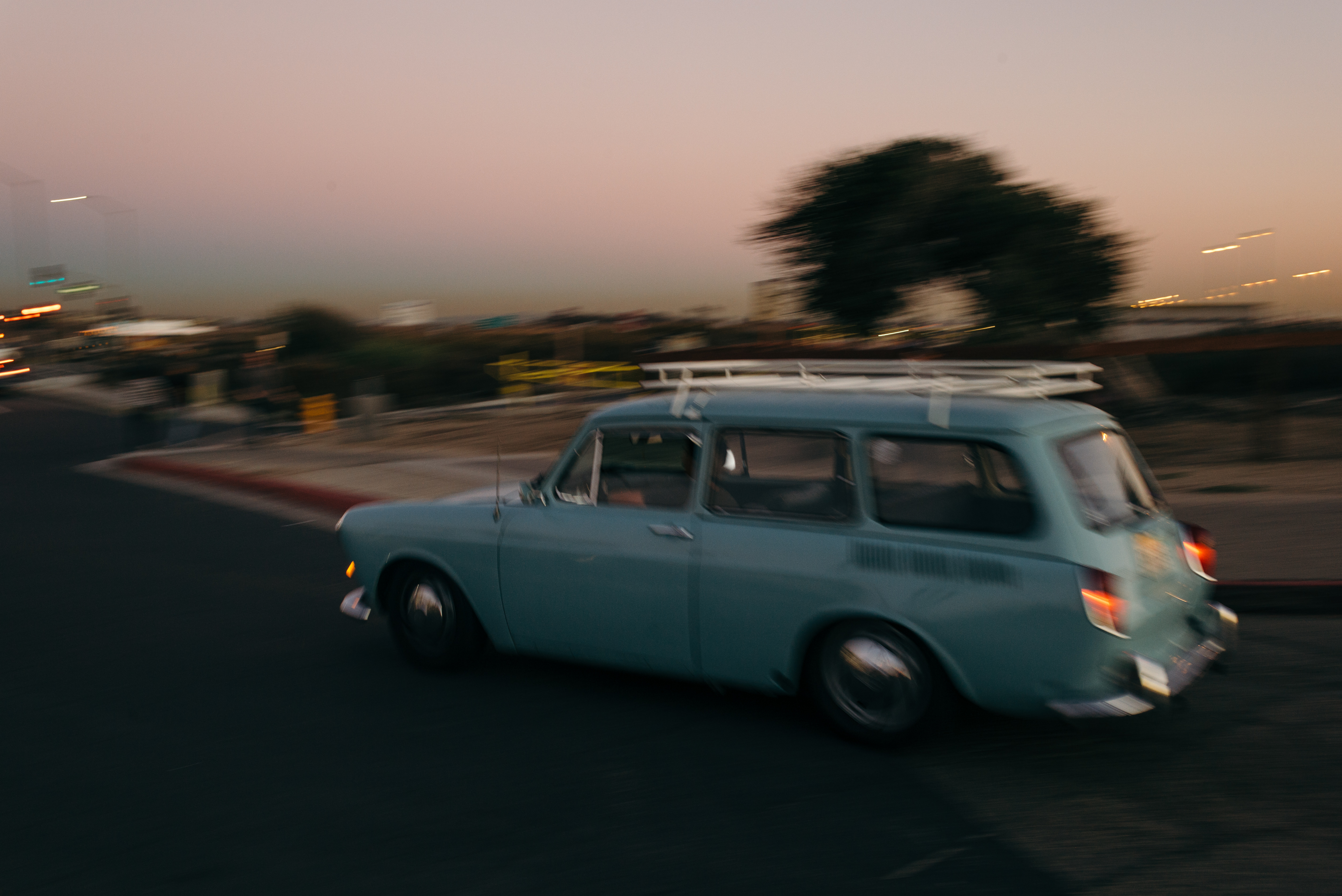 Motion blur of a vintage light blue station wagon with a white roof rack speeding past at sunset.