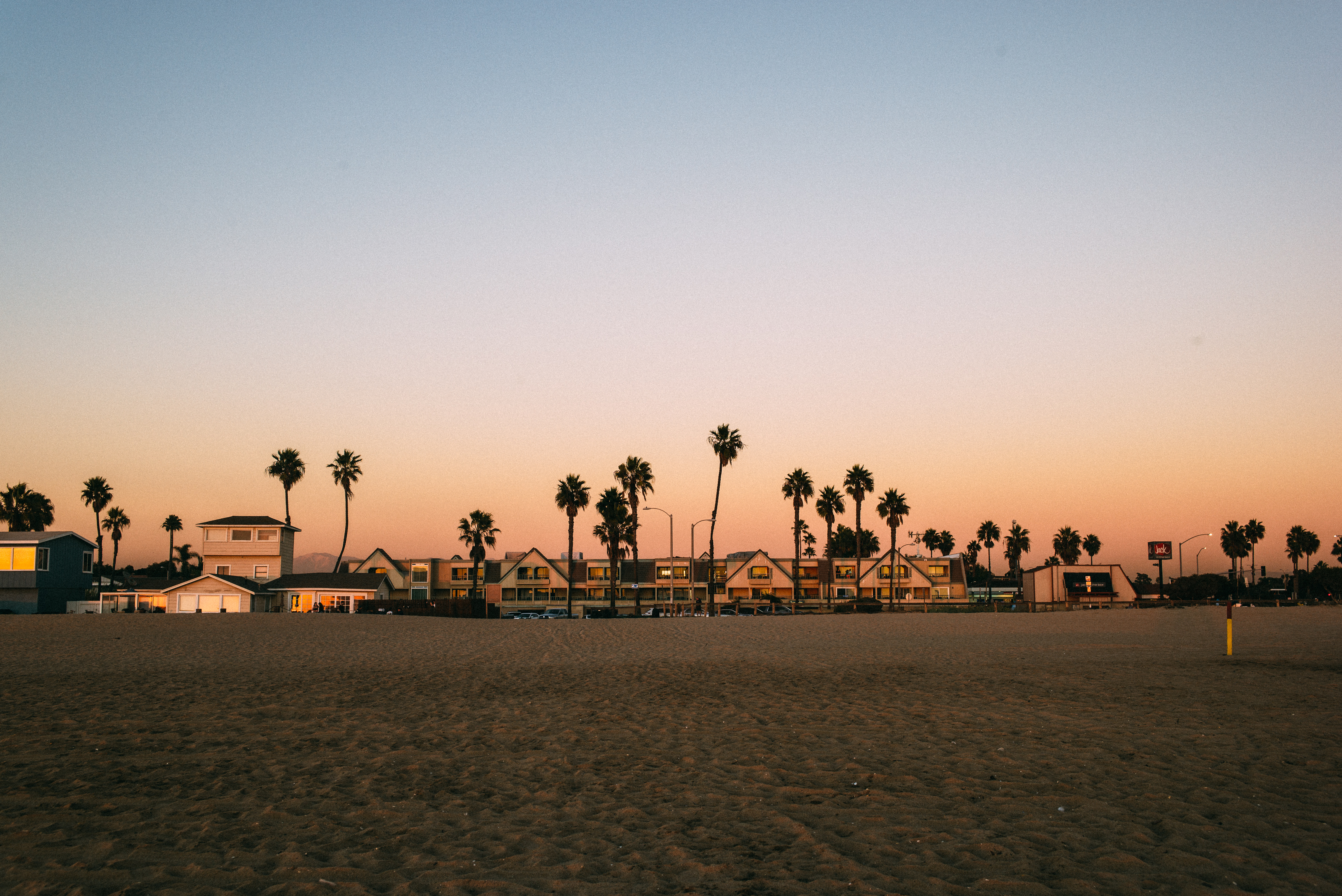 Sandy beach looking toward oceanfront condos and silhouetted palm trees beneath a peach sunset sky.