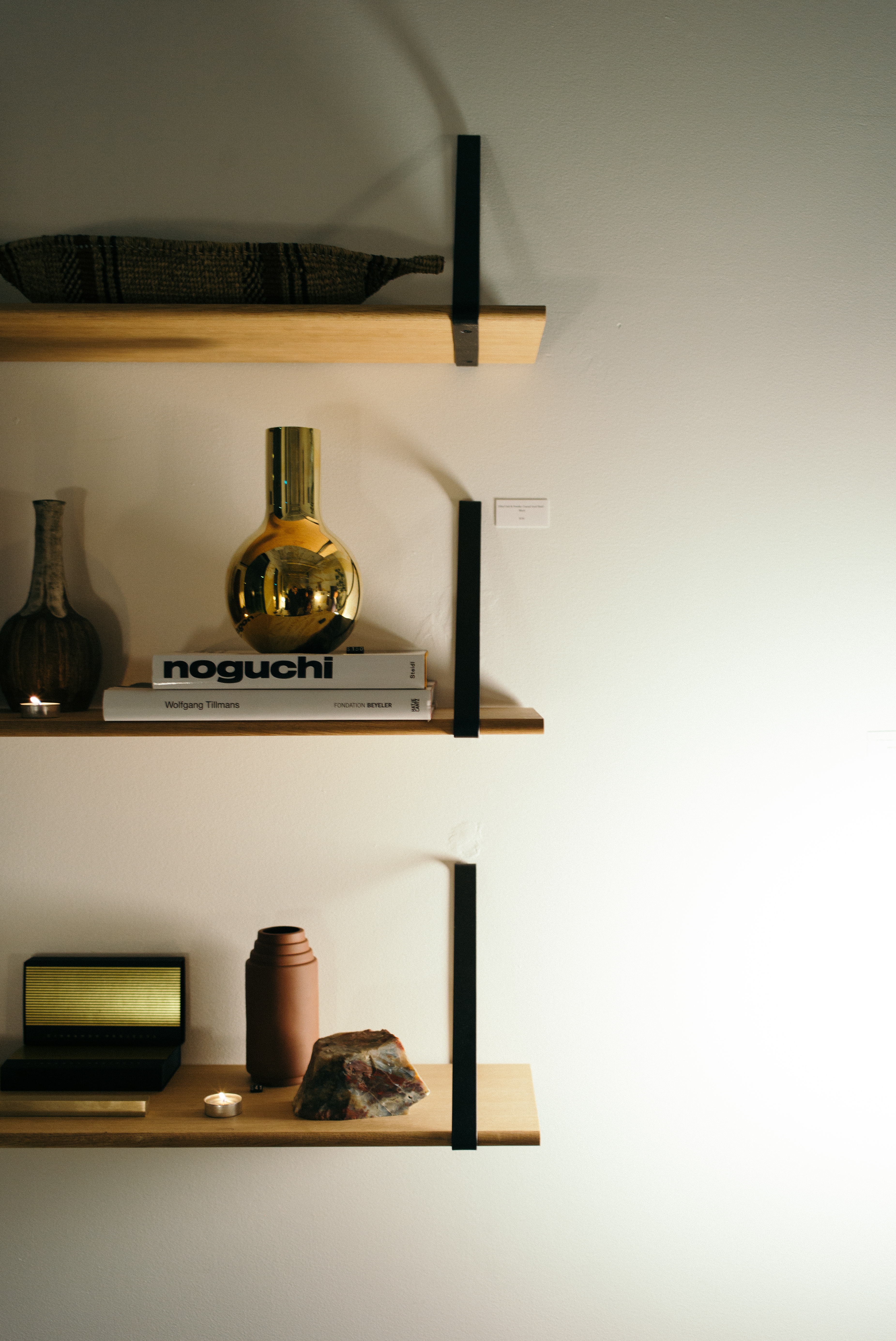 Wall shelves displaying 'noguchi' and 'Wolfgang Tillmans' art books with a brass vase, flowers, and candles.