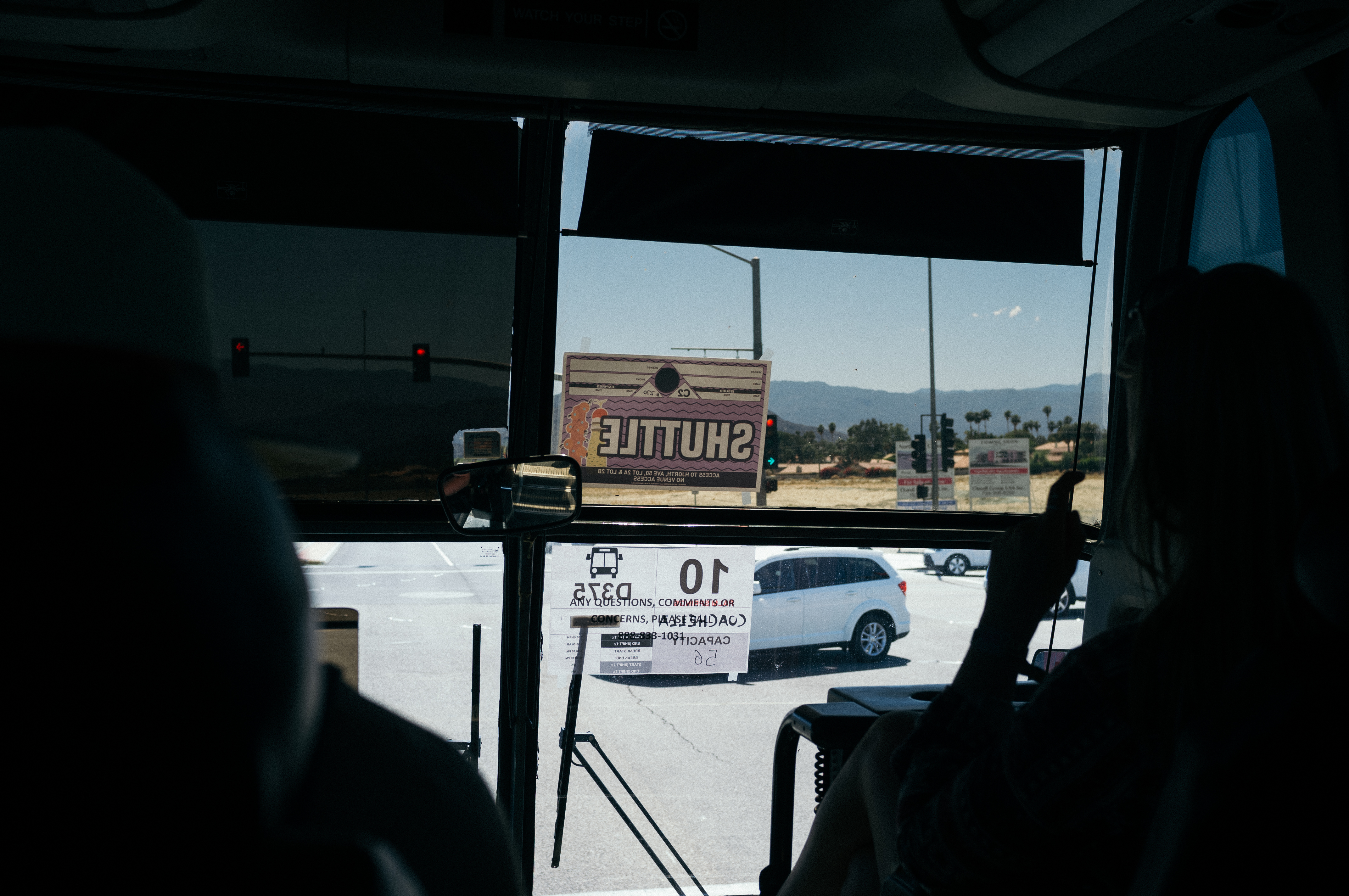 Desert highway lined with palm trees leading toward festival grounds at Coachella seen through a bus window.