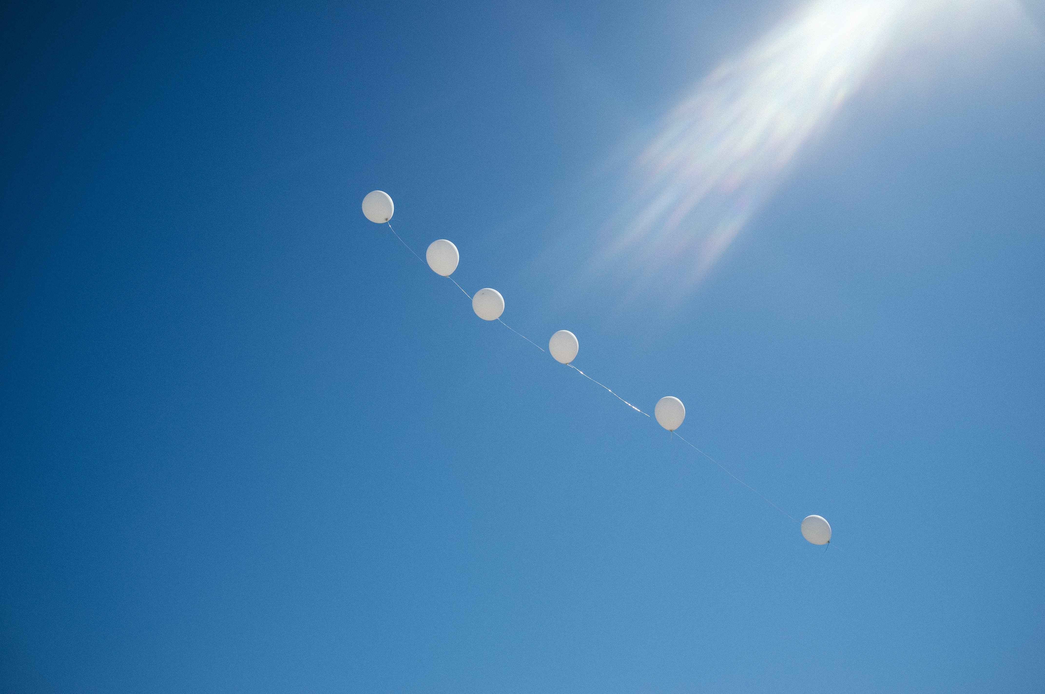 Arch of large white helium balloons floating high into a clear desert sky above Coachella festival grounds.