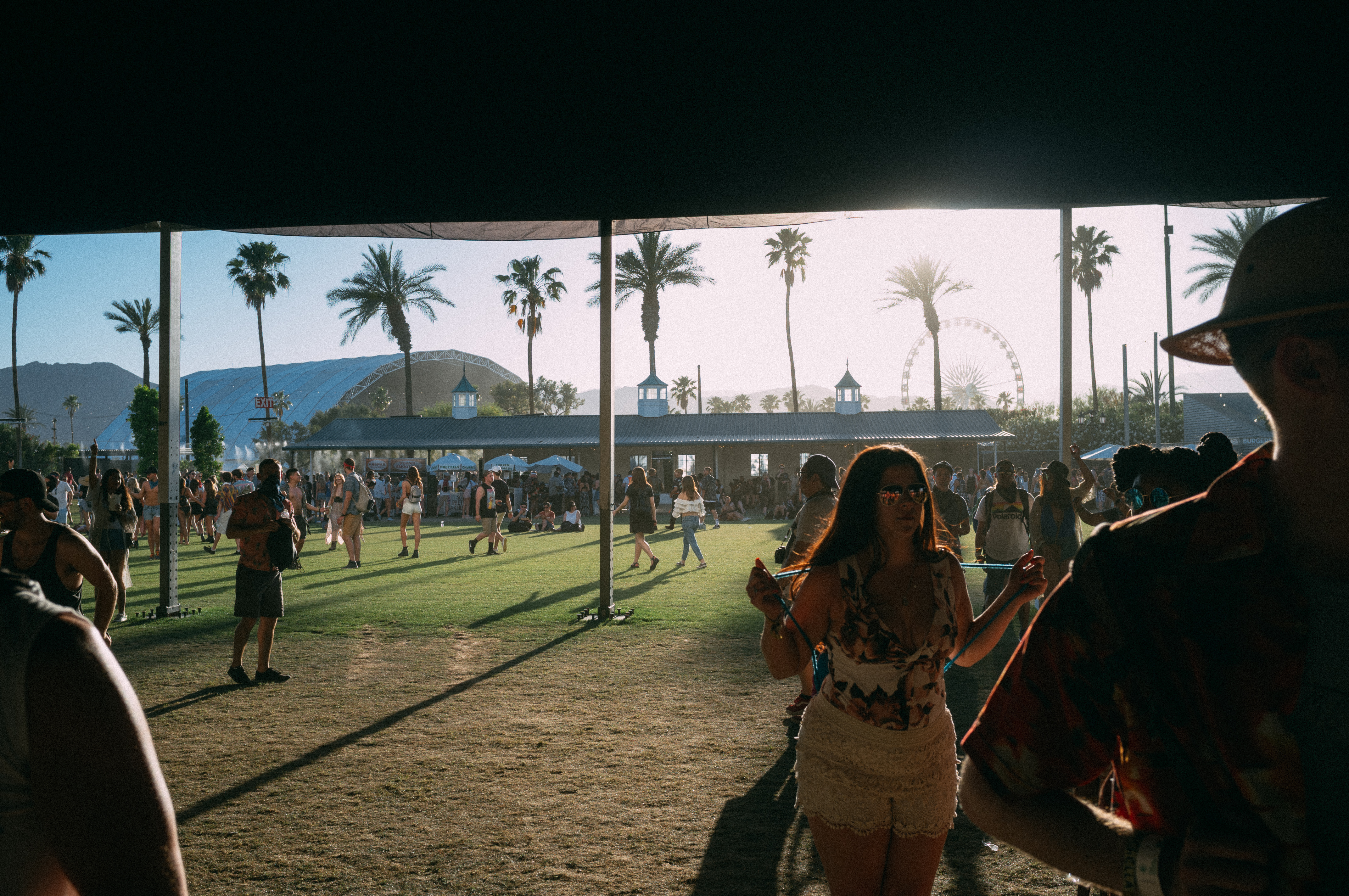 Attendees stroll past a rainbow geometric pavilion and shade tent on the Coachella festival grounds.