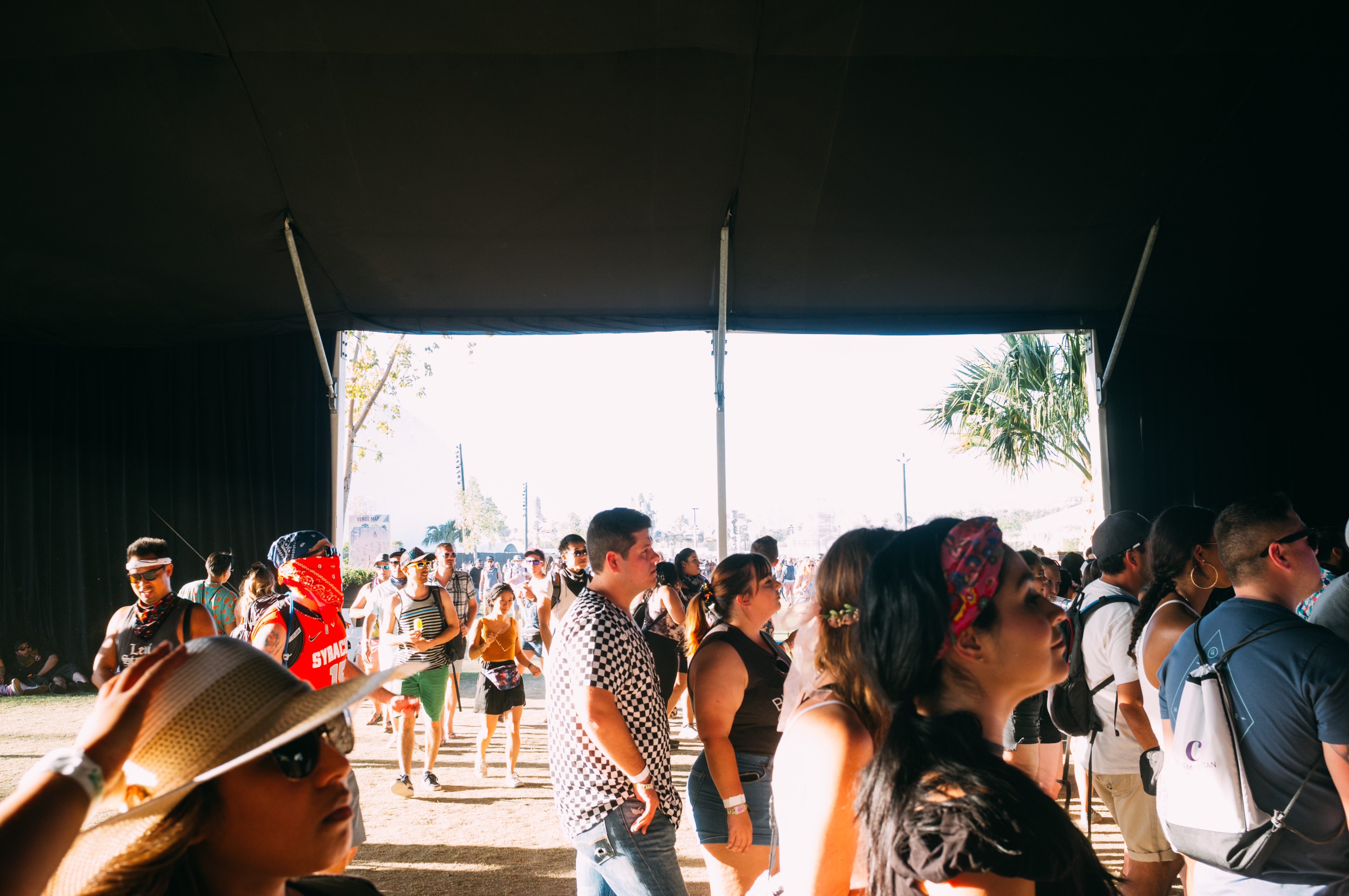 Festivalgoers under a canopy look toward a giant art installation and palm trees at Coachella.