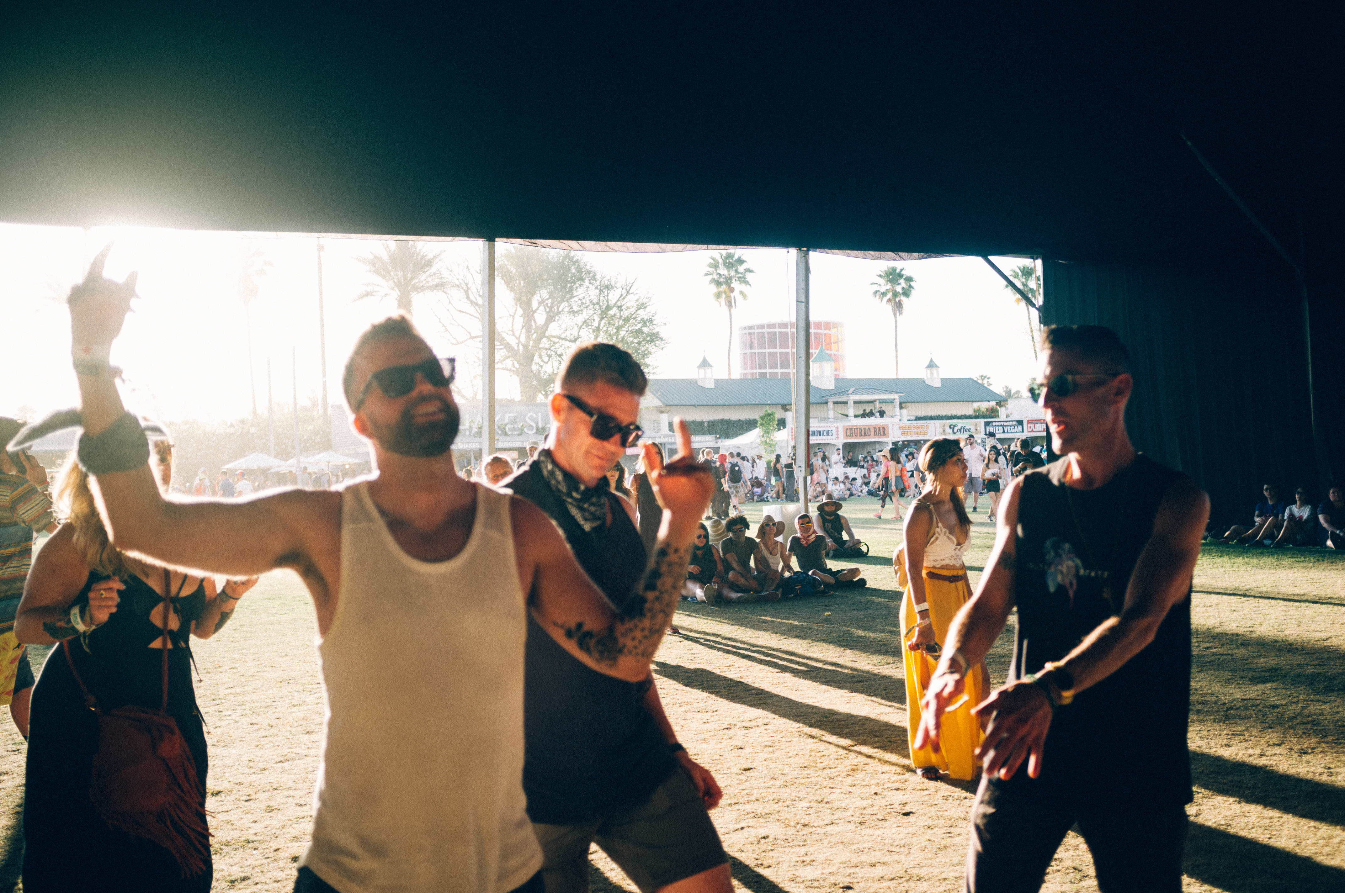 Friends laughing and dancing on the festival lawn bathed in warm golden-hour sunlight at Coachella.