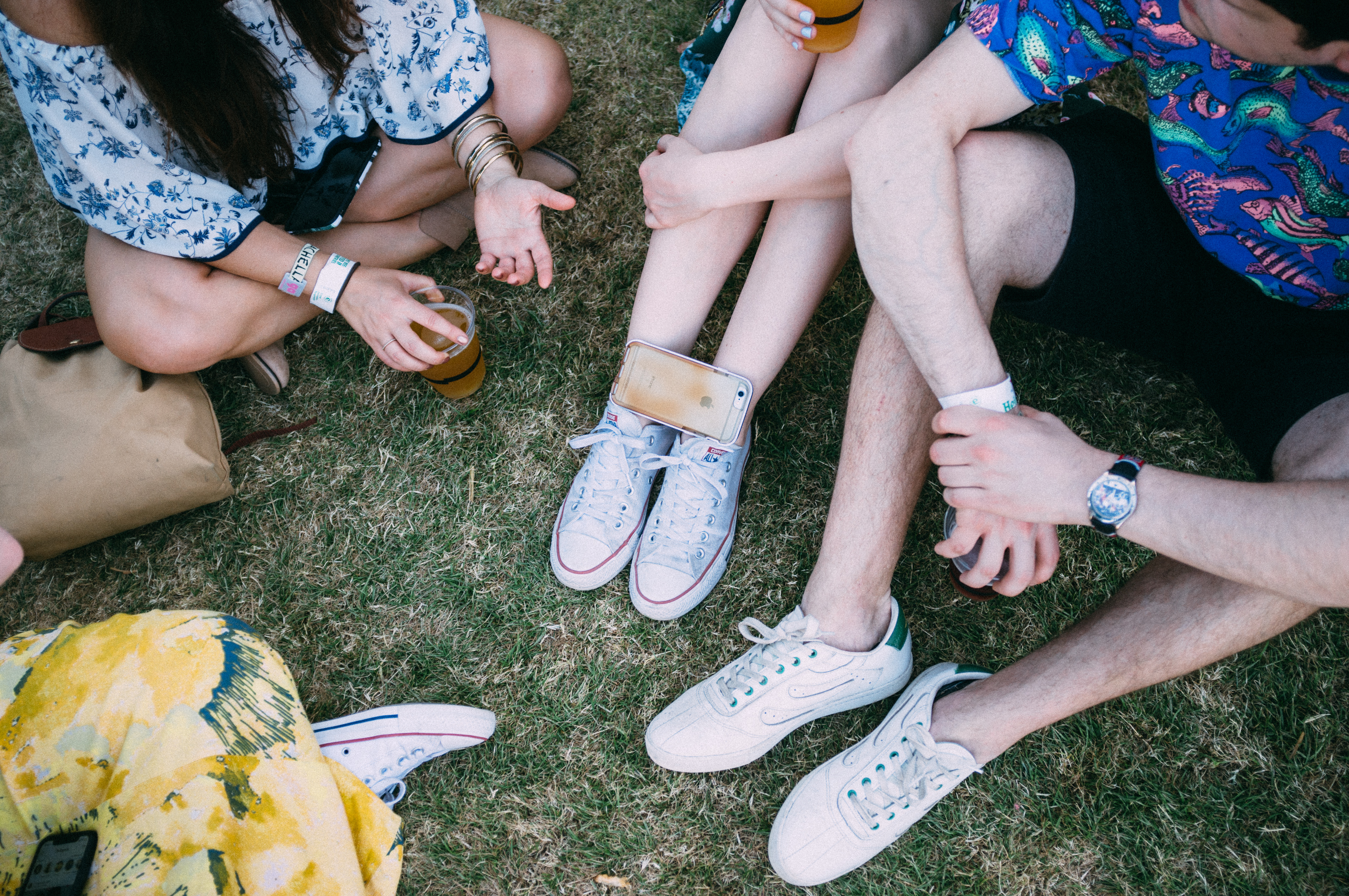 Friends sitting in a circle on the grassy lawn holding drinks and enjoying the afternoon sun at Coachella.