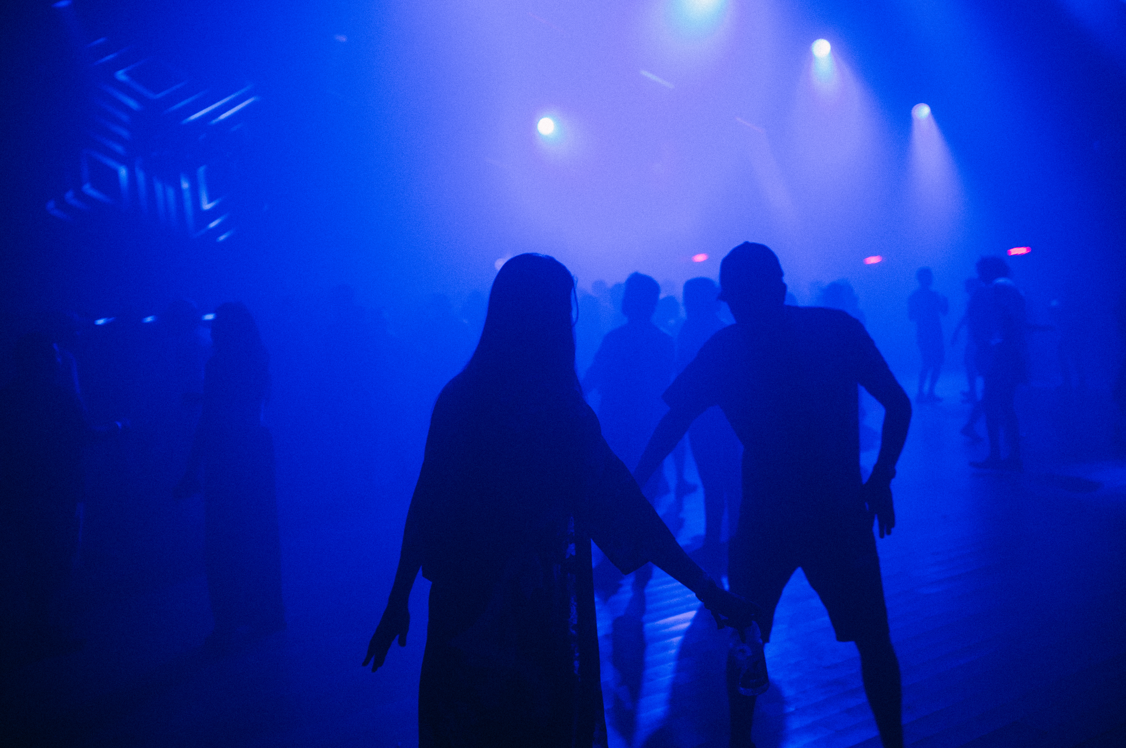 Concertgoers silhouetted before a blue illuminated stage with bright spotlights beaming at Coachella.