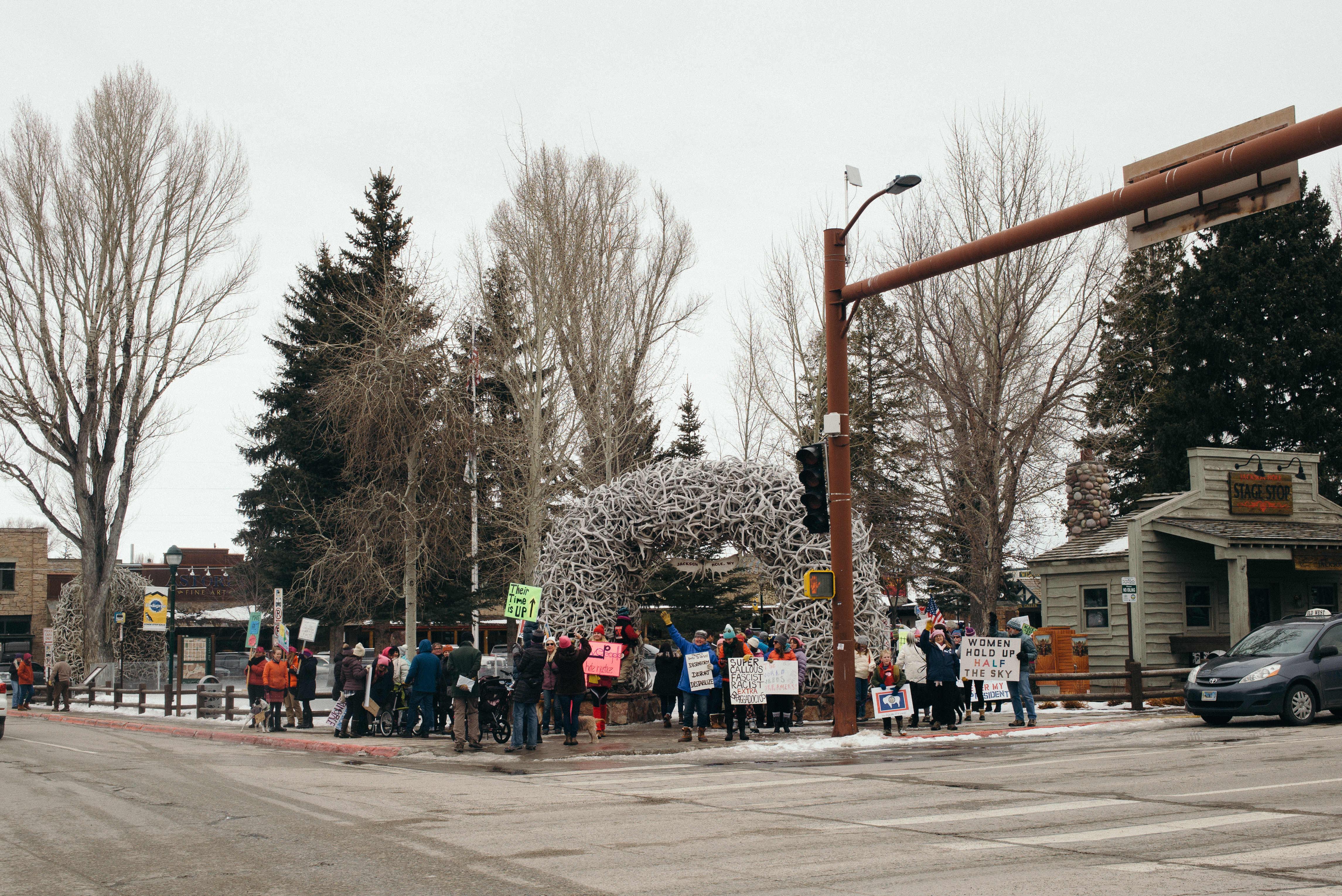 Rally attendees under the Jackson Hole elk antler arch holding signs like 'WOMEN HOLD UP HALF THE SKY'.