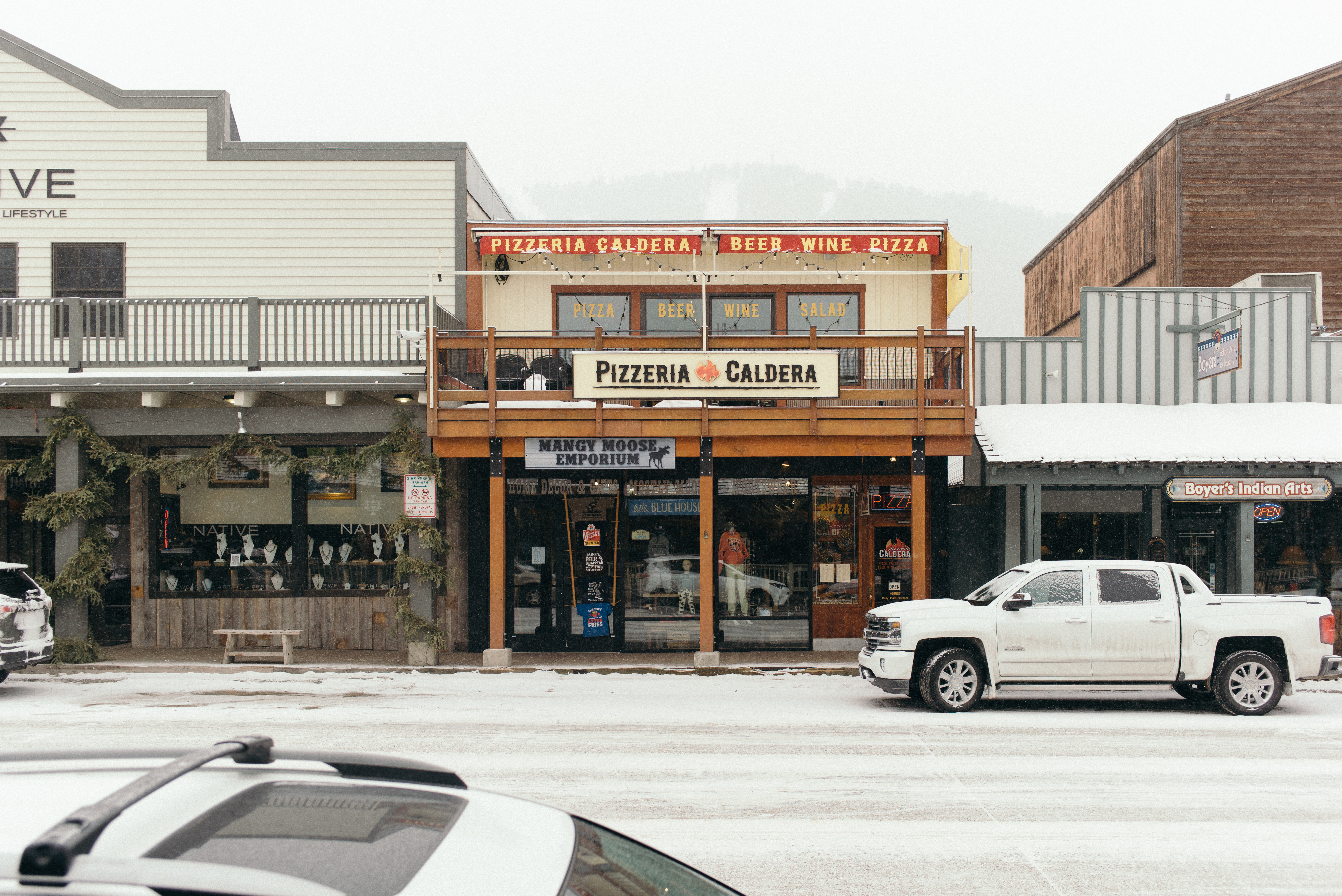Snowy street in Jackson Hole with a white pickup truck in front of Pizzeria Caldera and Mangy Moose.
