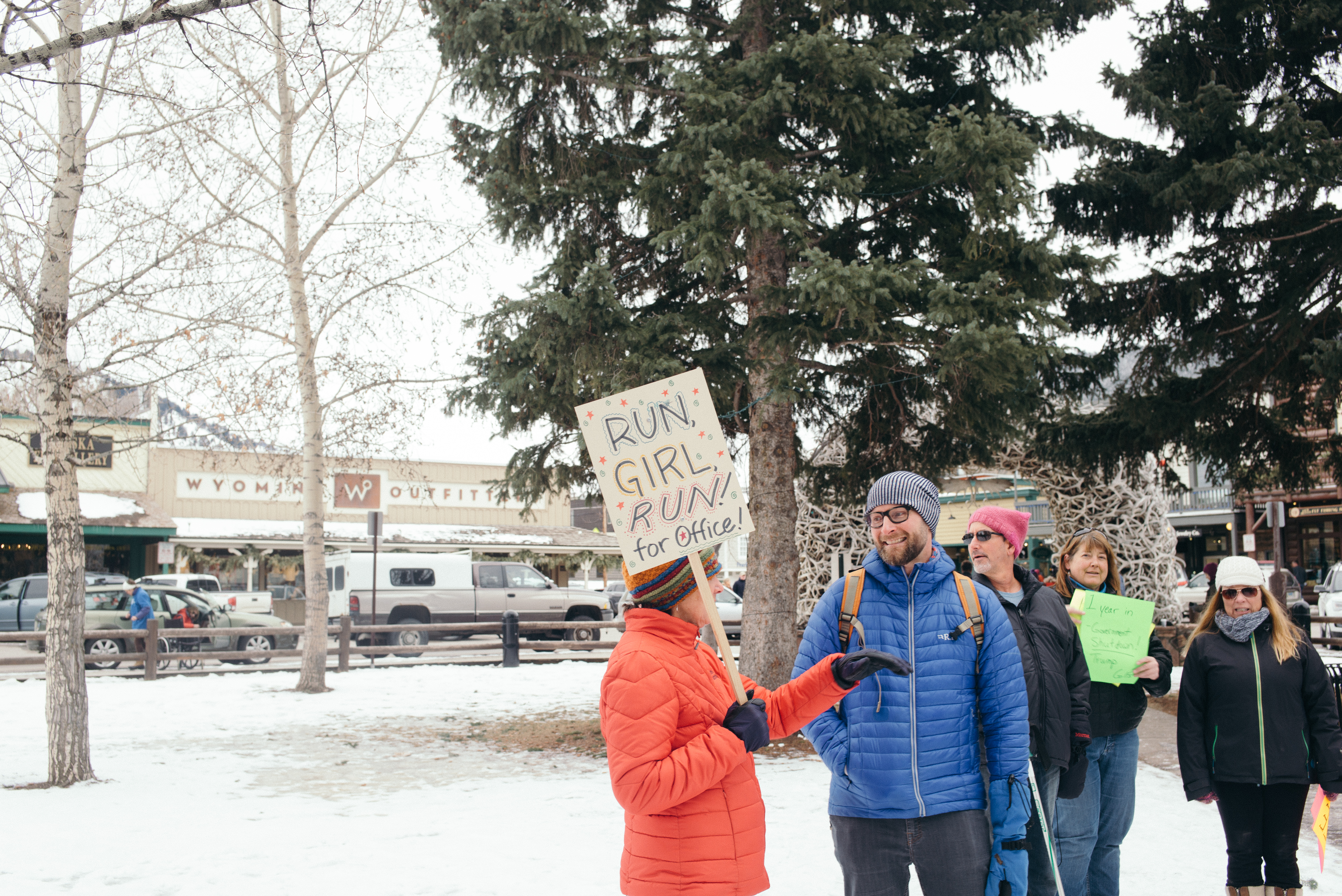 Demonstrator holding a 'RUN, GIRL, RUN! for Office!' sign speaks with an attendee at Jackson Hole Square.