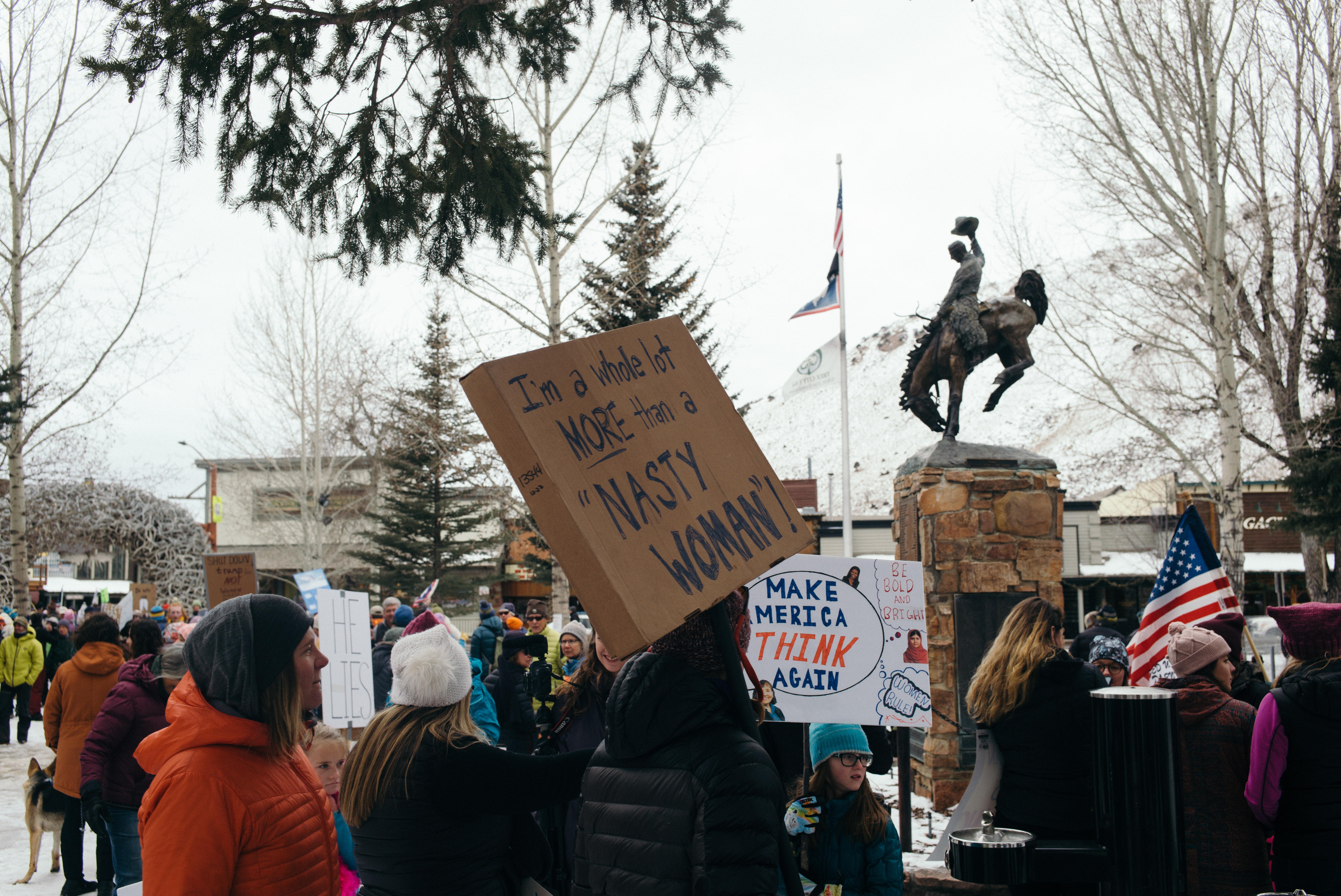 Rally attendees hold signs reading 'I'm a whole lot MORE than a NASTY WOMAN!' and 'MAKE MERICA THINK AGAIN'.