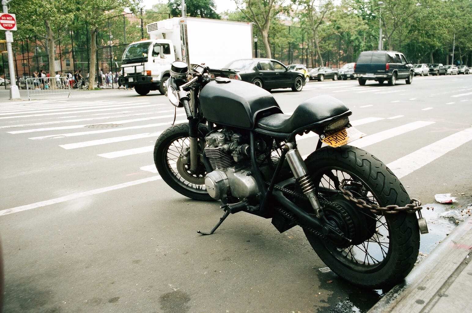 Matte black cafe racer motorcycle parked curbside with a heavy security chain wrapped through the wheel.
