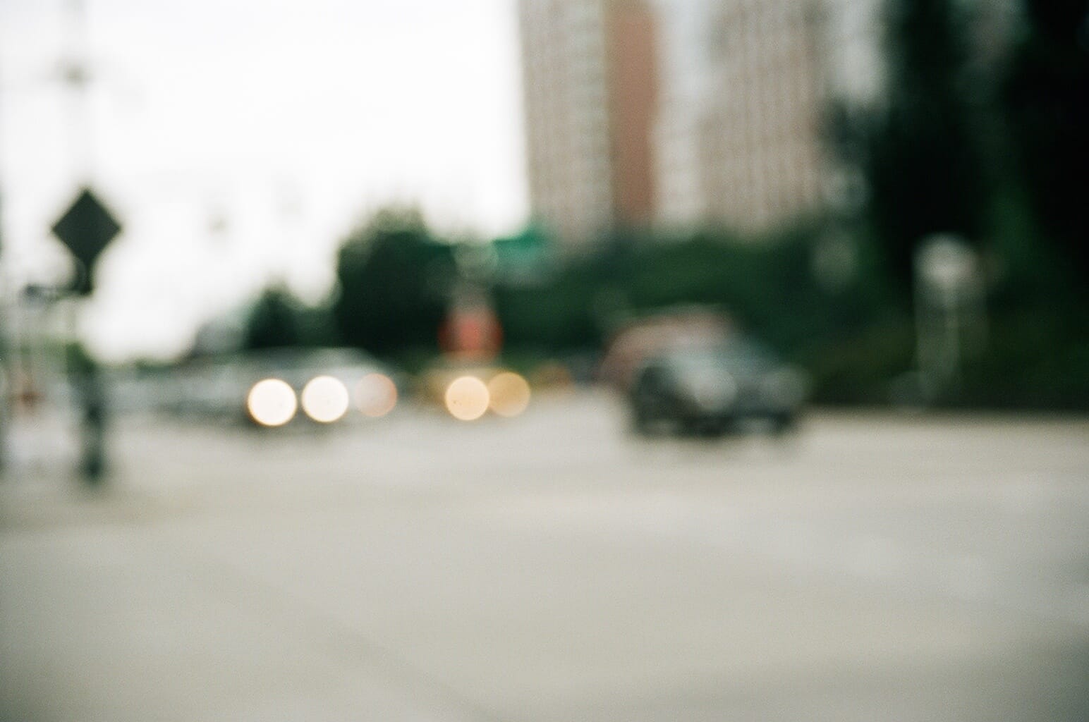 Soft out-of-focus view across an urban avenue showing blurry vehicle headlights and distant trees.