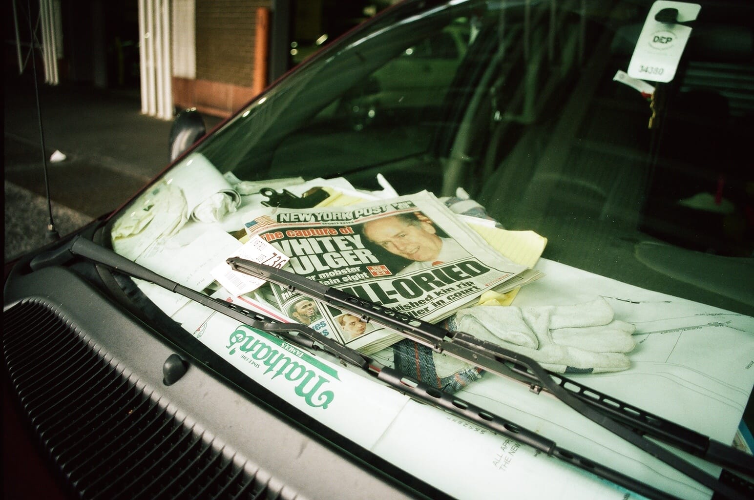 Vehicle dashboard cluttered with a New York Post on Whitey Bulger's capture, gloves, and a paper bag.
