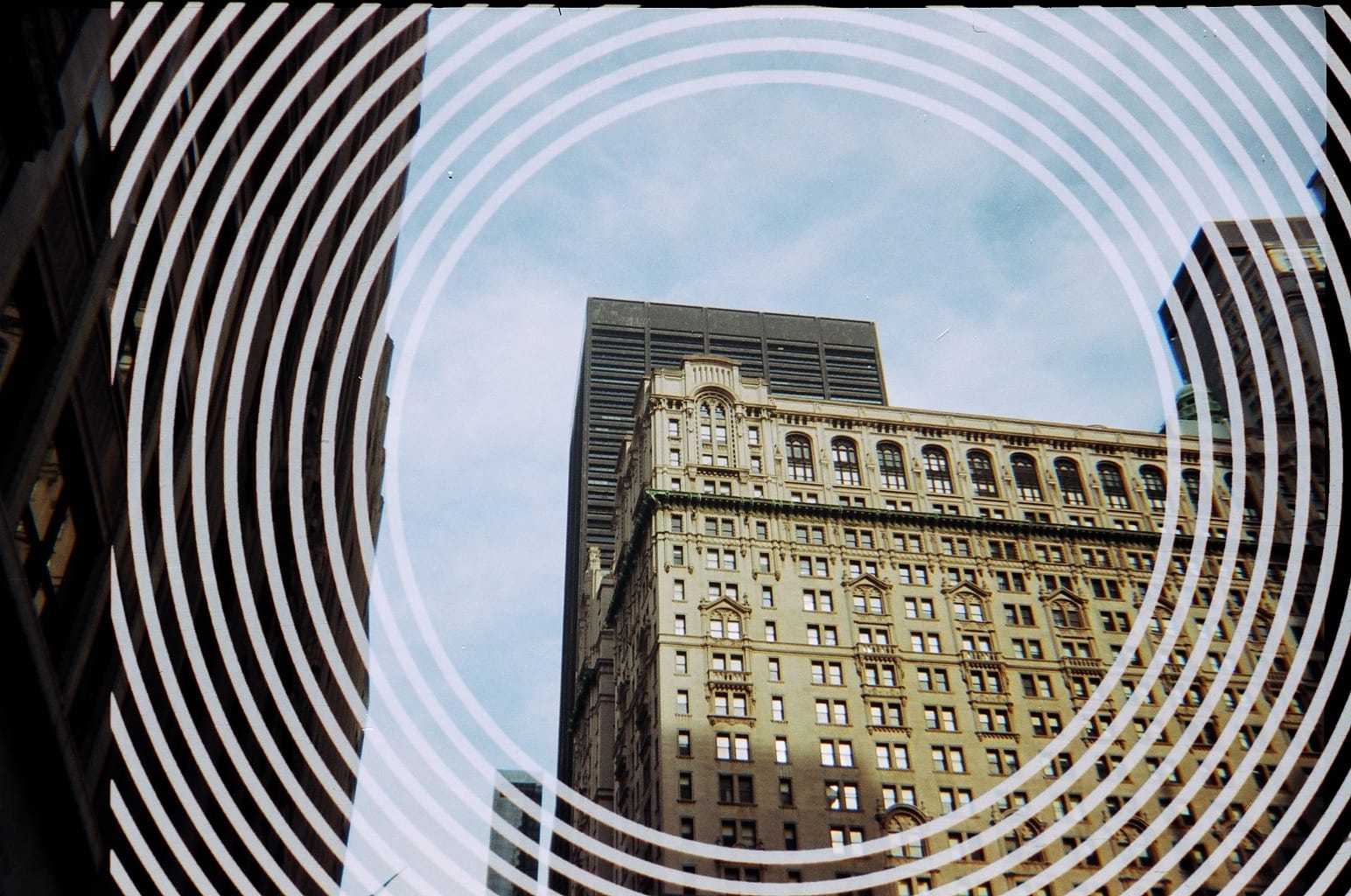 Low-angle view of Lower Manhattan historic skyscrapers overlaid with white hypnotic concentric circles.