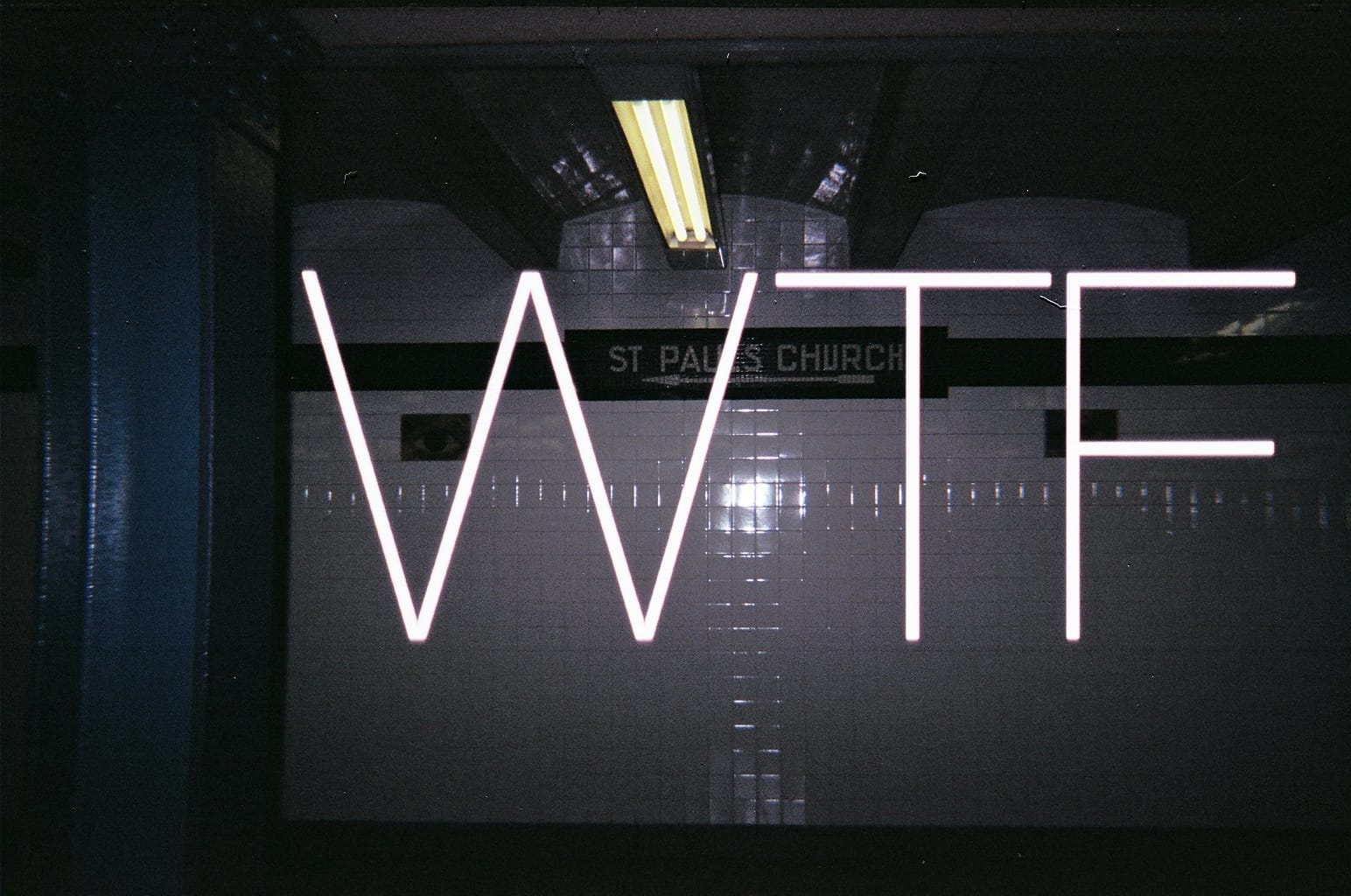 Subway wall with St Paul's Church directional sign and glowing white letters spelling 'WTF' superimposed.