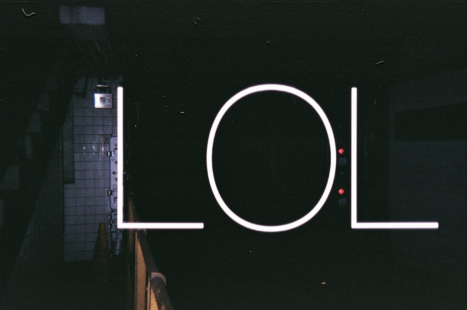Nocturnal view looking into a dark subway tunnel with large glowing white letters spelling 'LOL' superimposed.