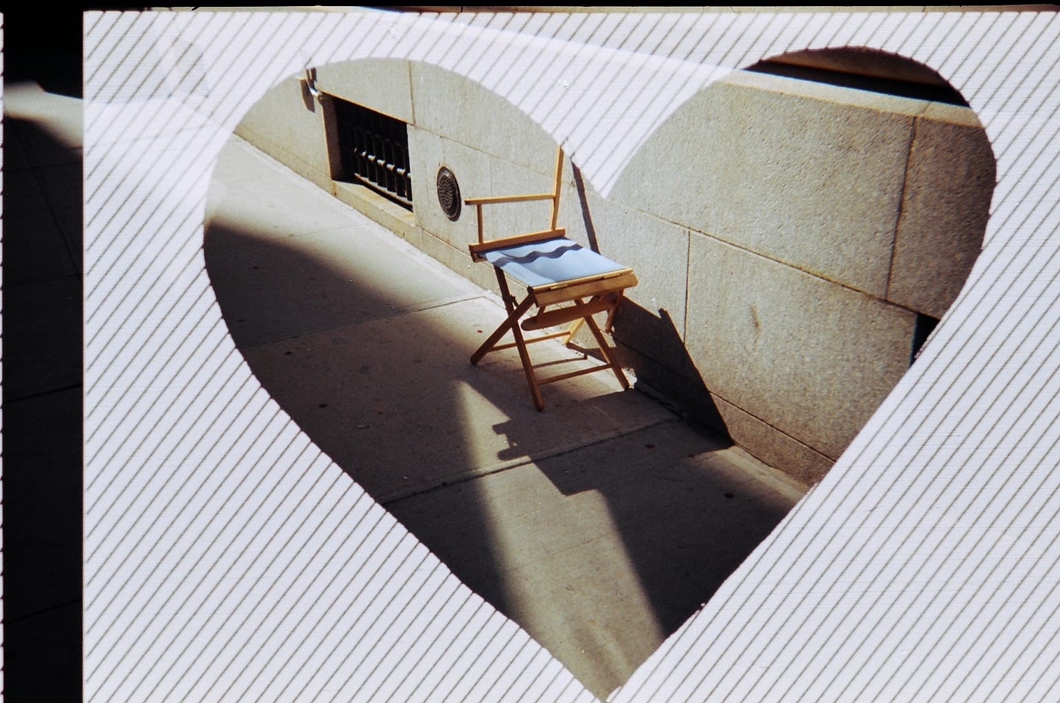 Sunlit folding director's chair on a sidewalk framed within a heart-shaped vignette border.
