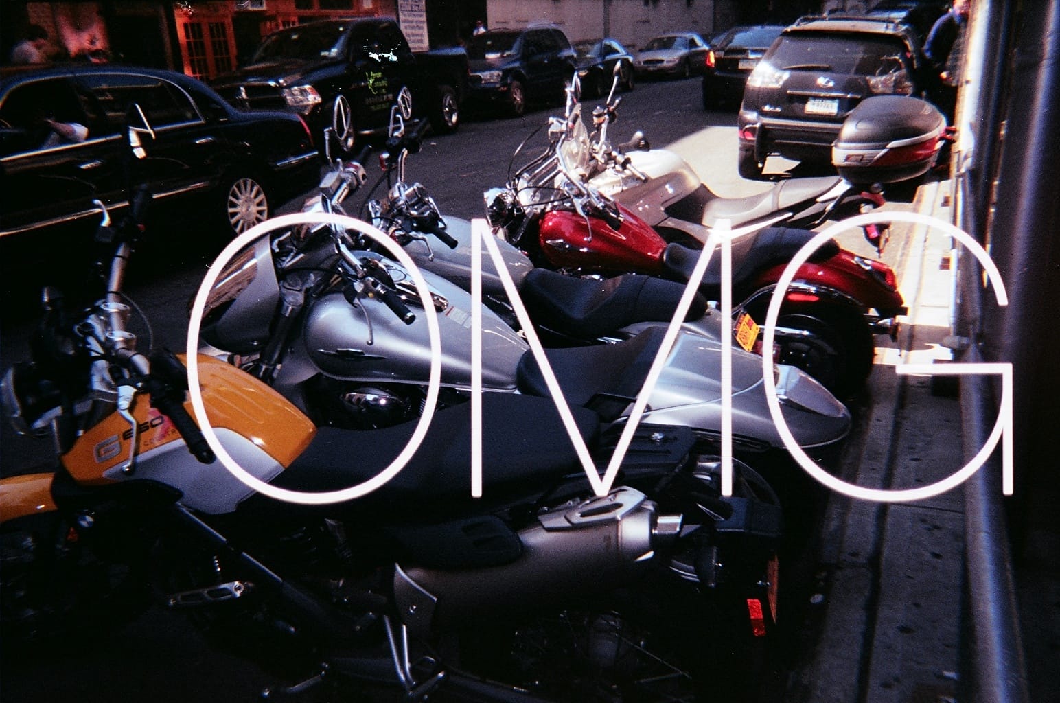 Parked motorcycles along a city street with large white glowing letters spelling 'OMG' superimposed.