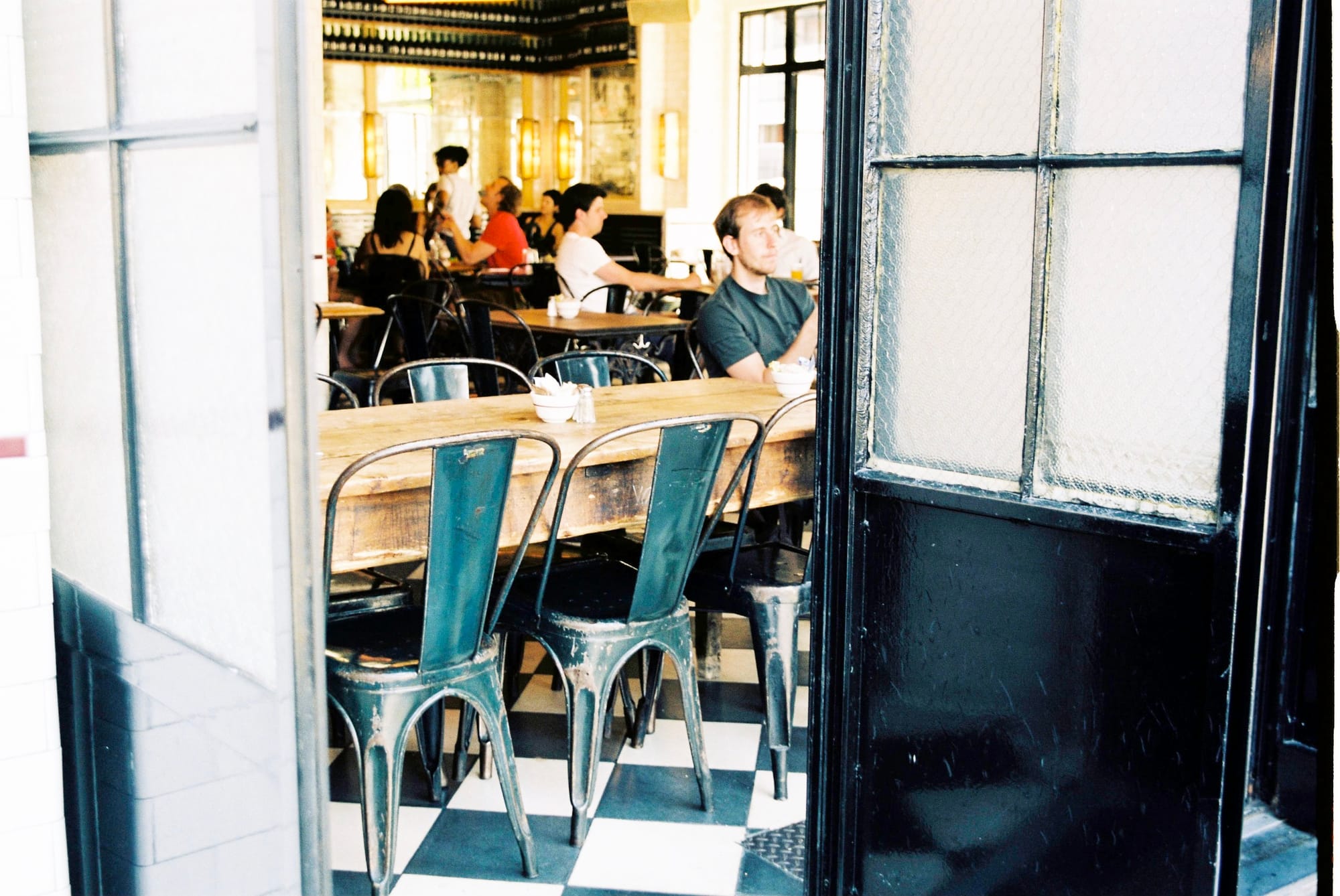 Looking through an open industrial doorway into a bright cafe with checkered floors and green metal chairs.