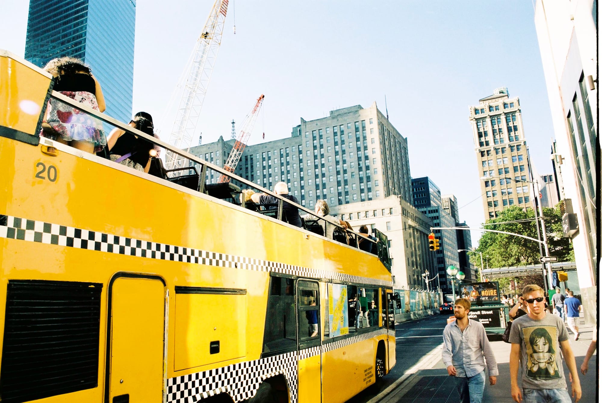 Low-angle view of a yellow open-top double-decker tour bus in Lower Manhattan with skyscrapers behind.