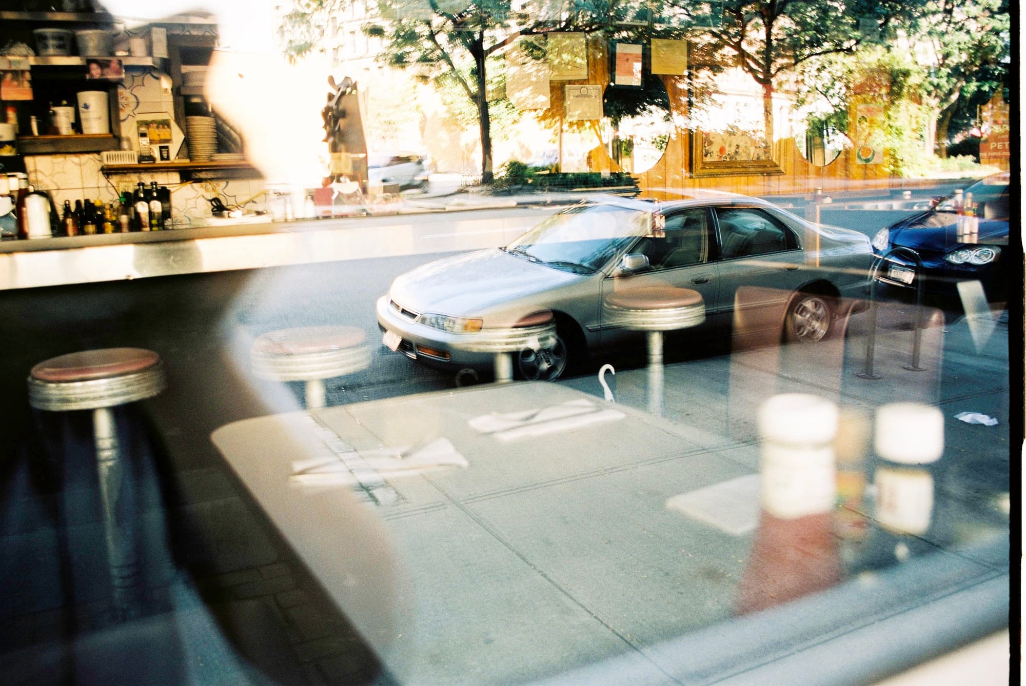 Layered reflection through a diner window blending counter stools and condiment bottles with the street.
