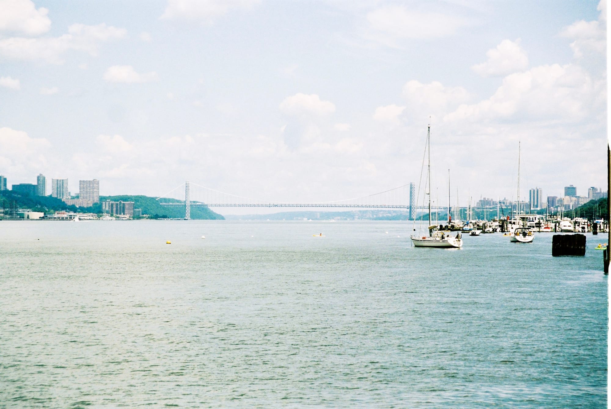 Scenic view up the Hudson River toward the George Washington Bridge with moored sailboats in foreground.