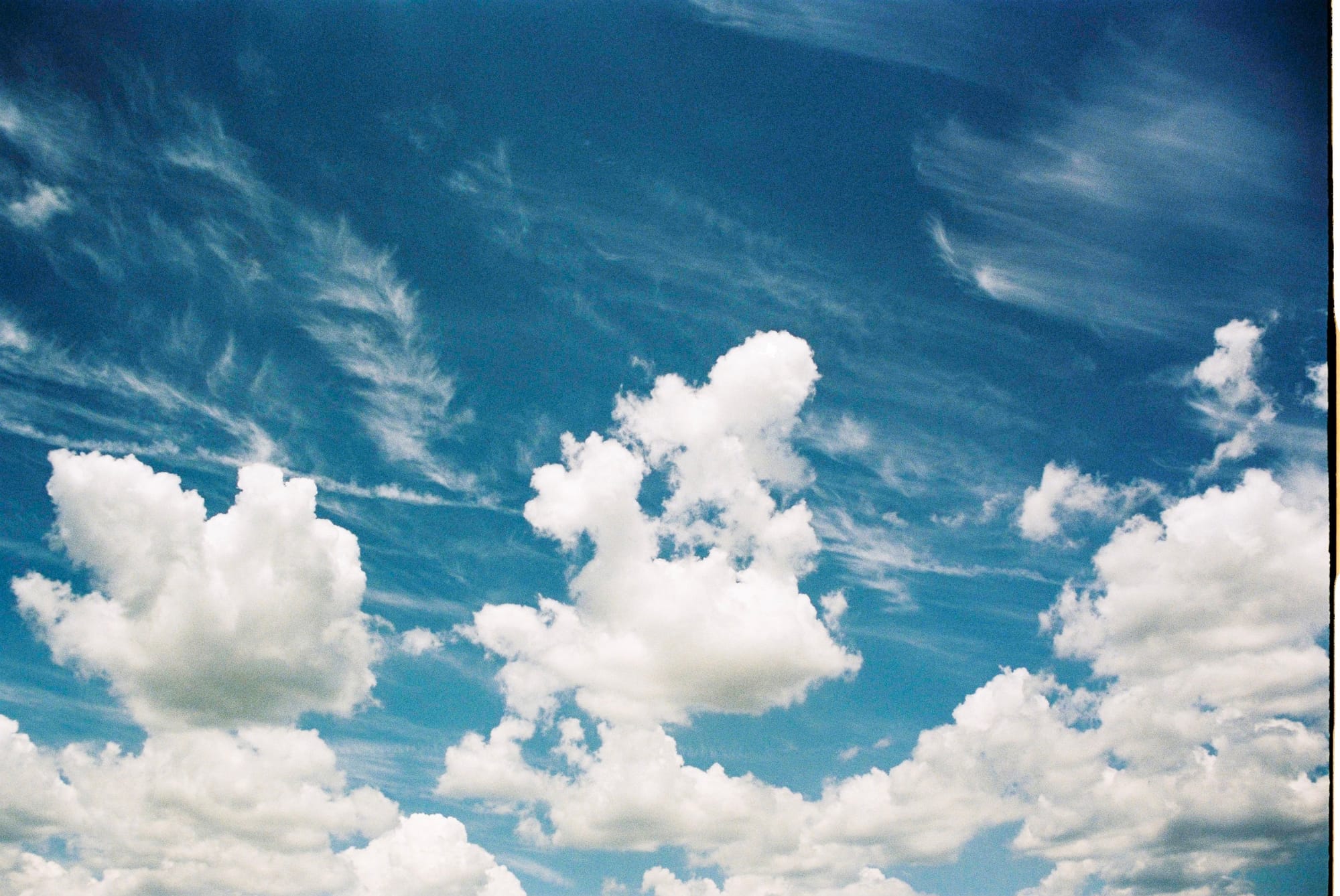 Expansive cloudscape of white cumulus clouds drifting across a deep blue summer sky.