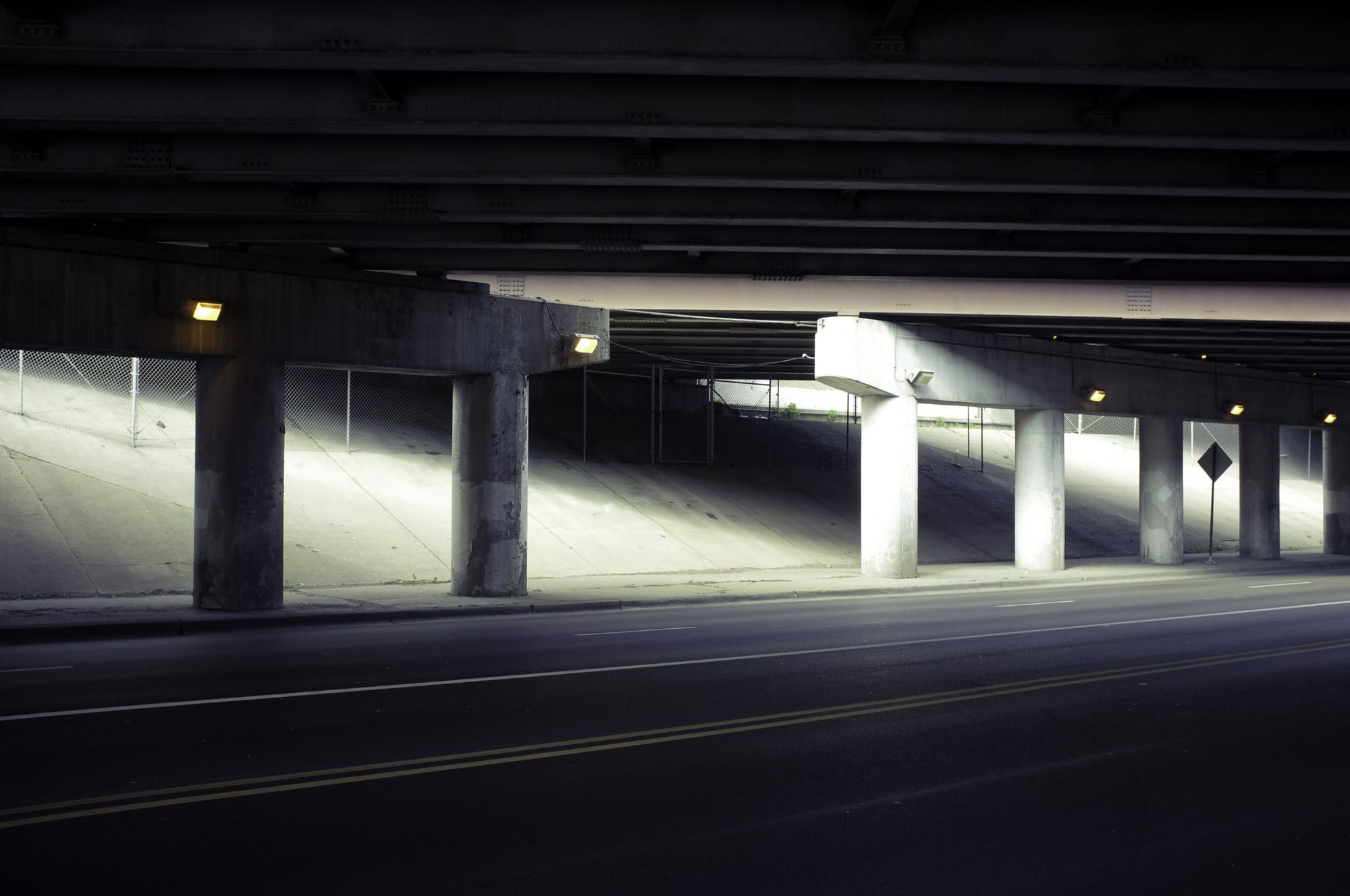 Atmospheric perspective through concrete pillars beneath an airport overpass with light beams.