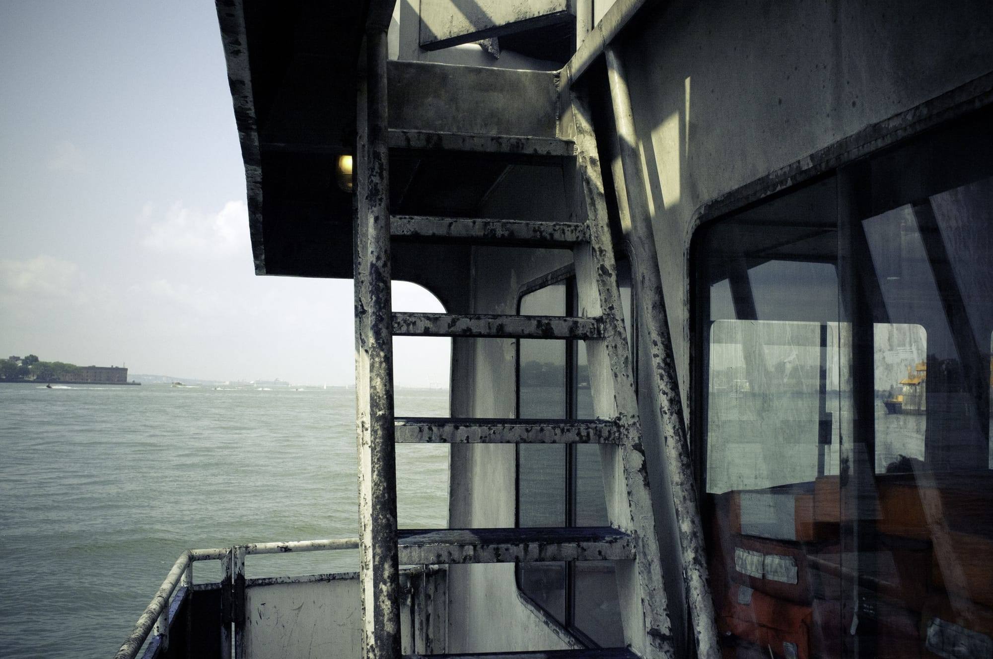 View from the deck of Governors Island ferry past a metal companionway ladder toward New York Harbor.