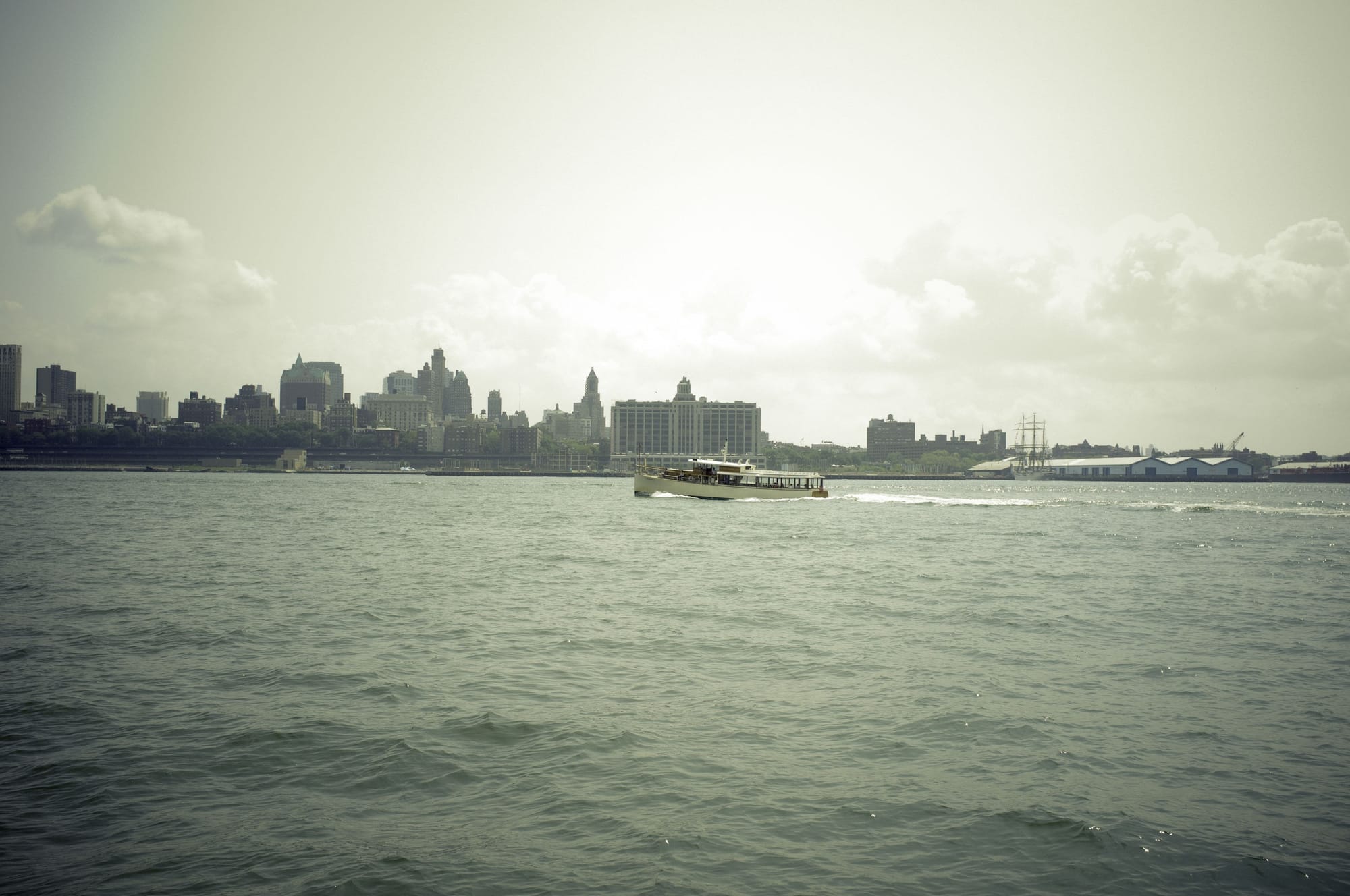 Classic wooden tour ferry cruising New York Harbor toward the distant Brooklyn waterfront skyline.
