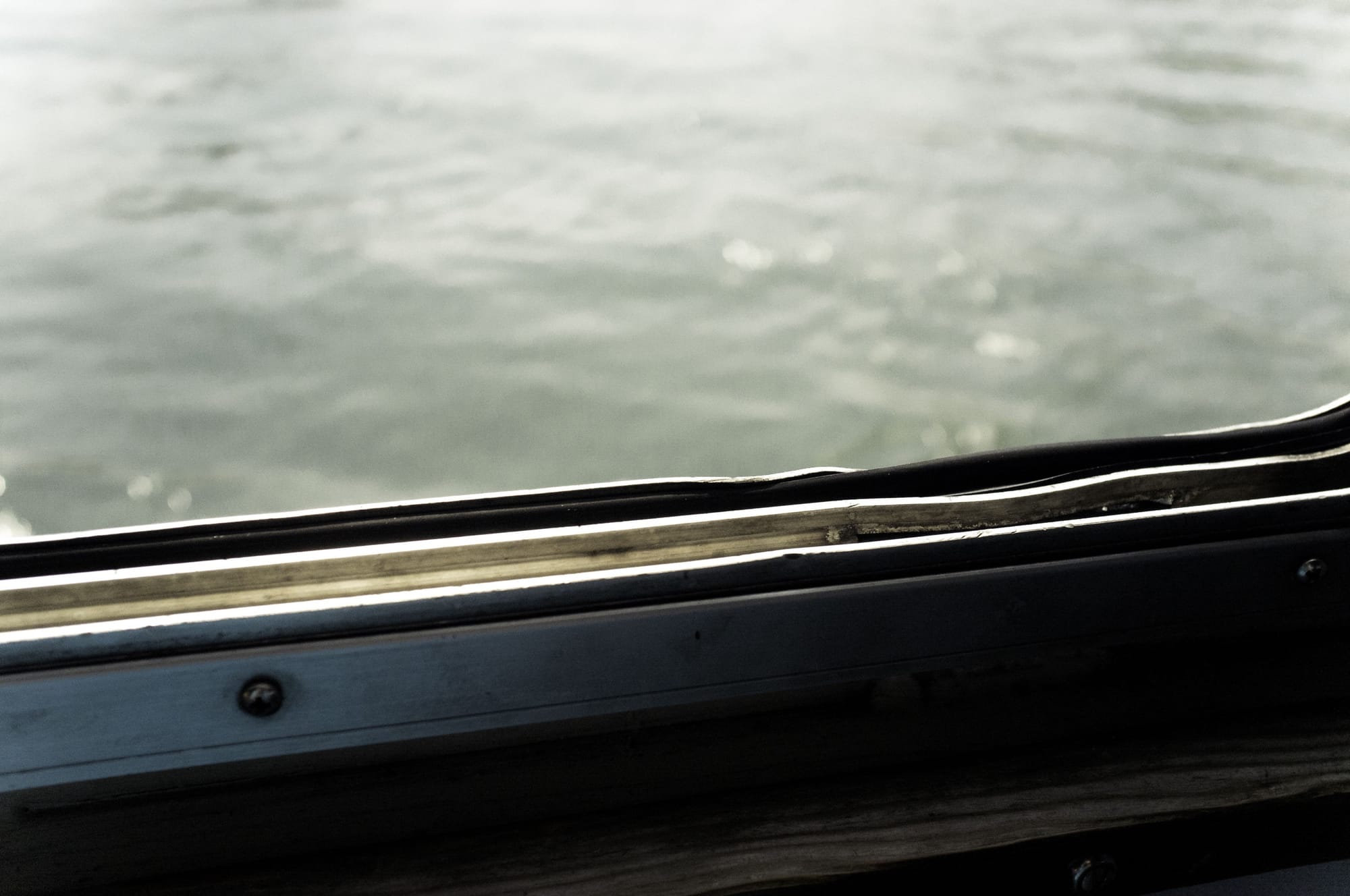 Worn metal ferry window frame overlooking the calm greenish water of New York Harbor.