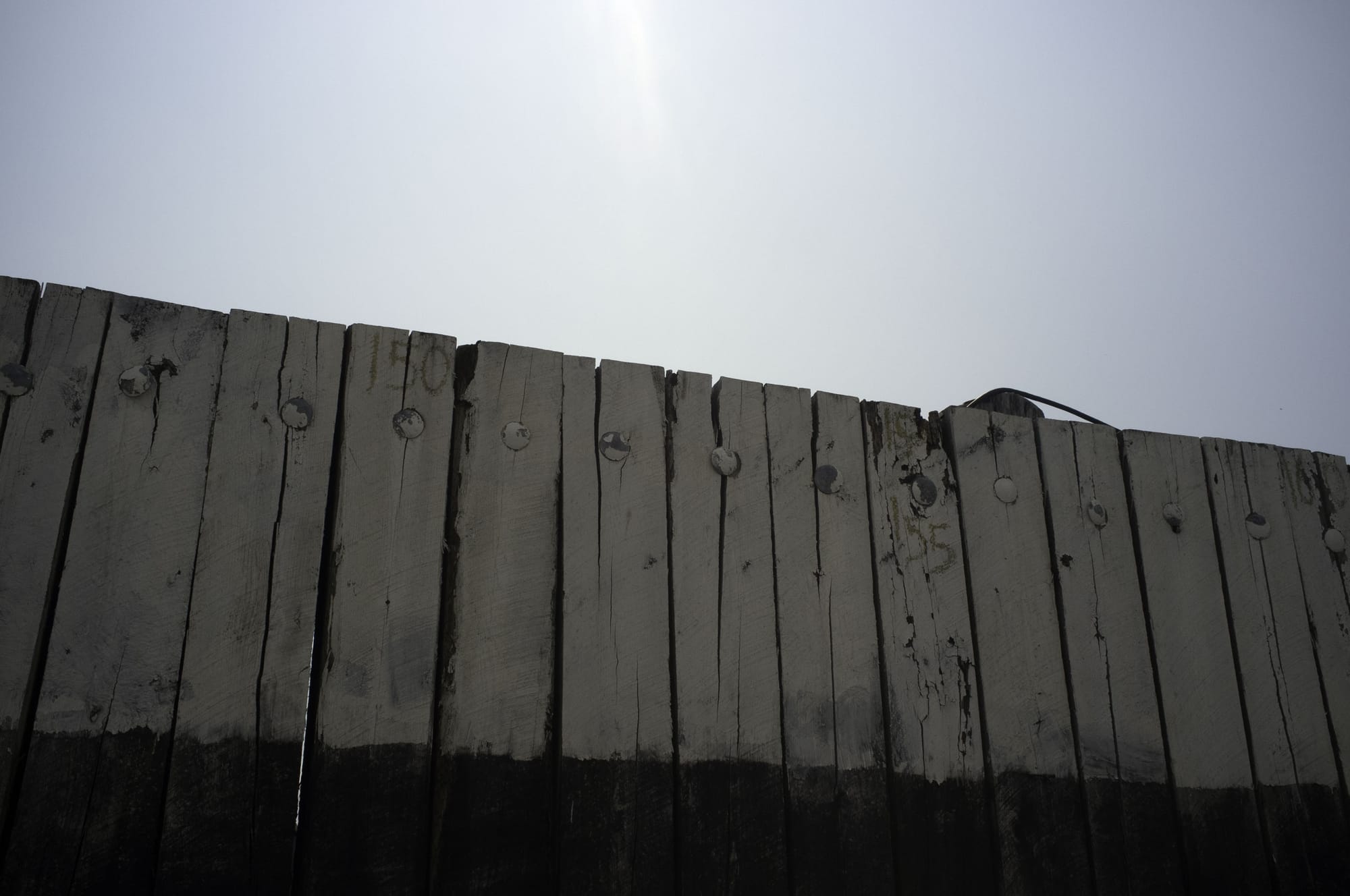 Weathered wooden ferry pier wall painted white and black with heavy metal bolts against a blue sky.