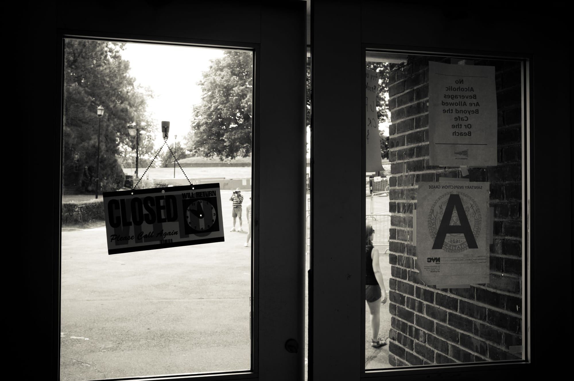 Glass doors on Governors Island displaying a 'CLOSED' sign and grade 'A' placard beside brick pillars.