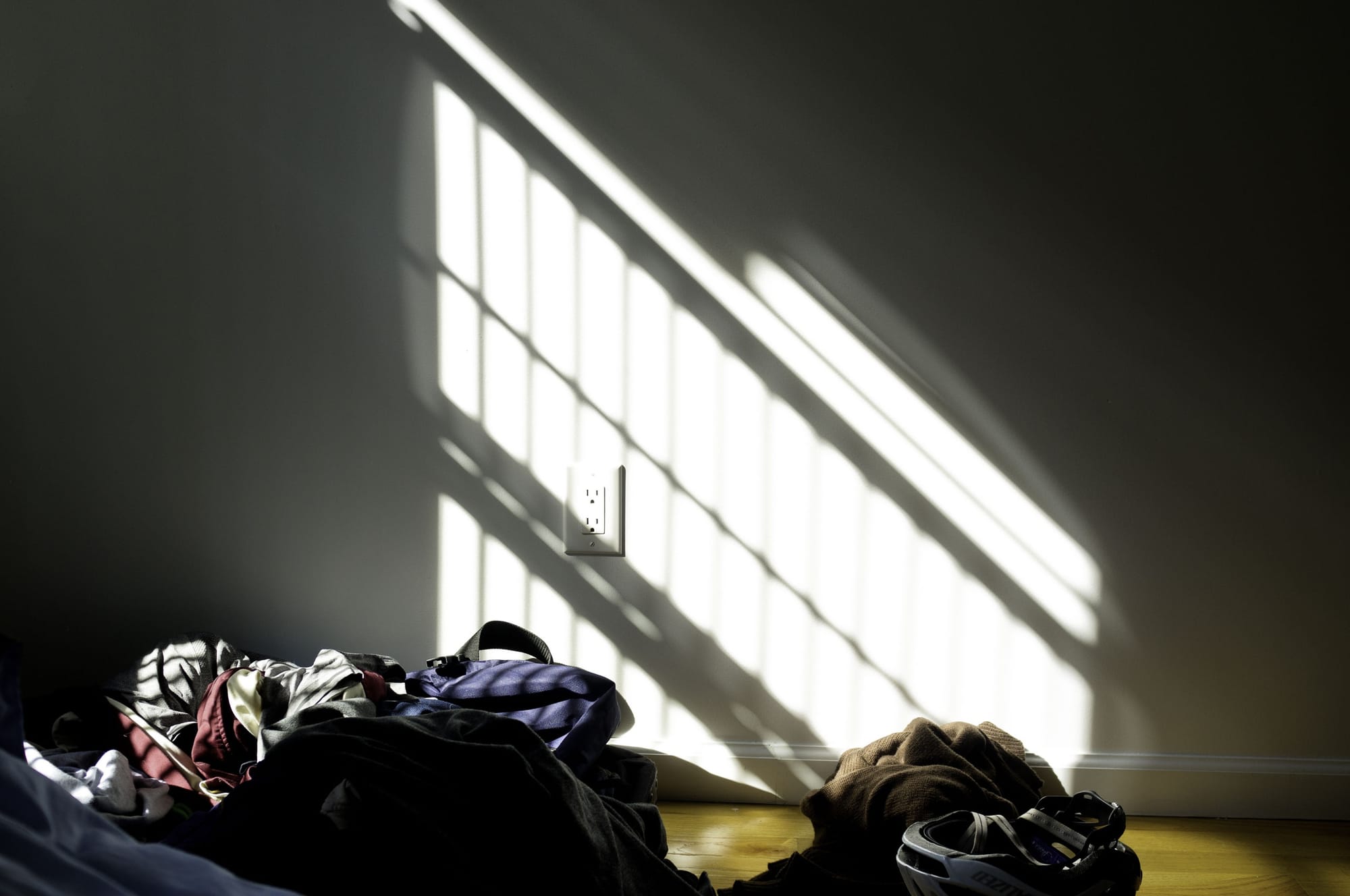 Strong diagonal sunbeams streaming through window blinds across a hardwood floor.
