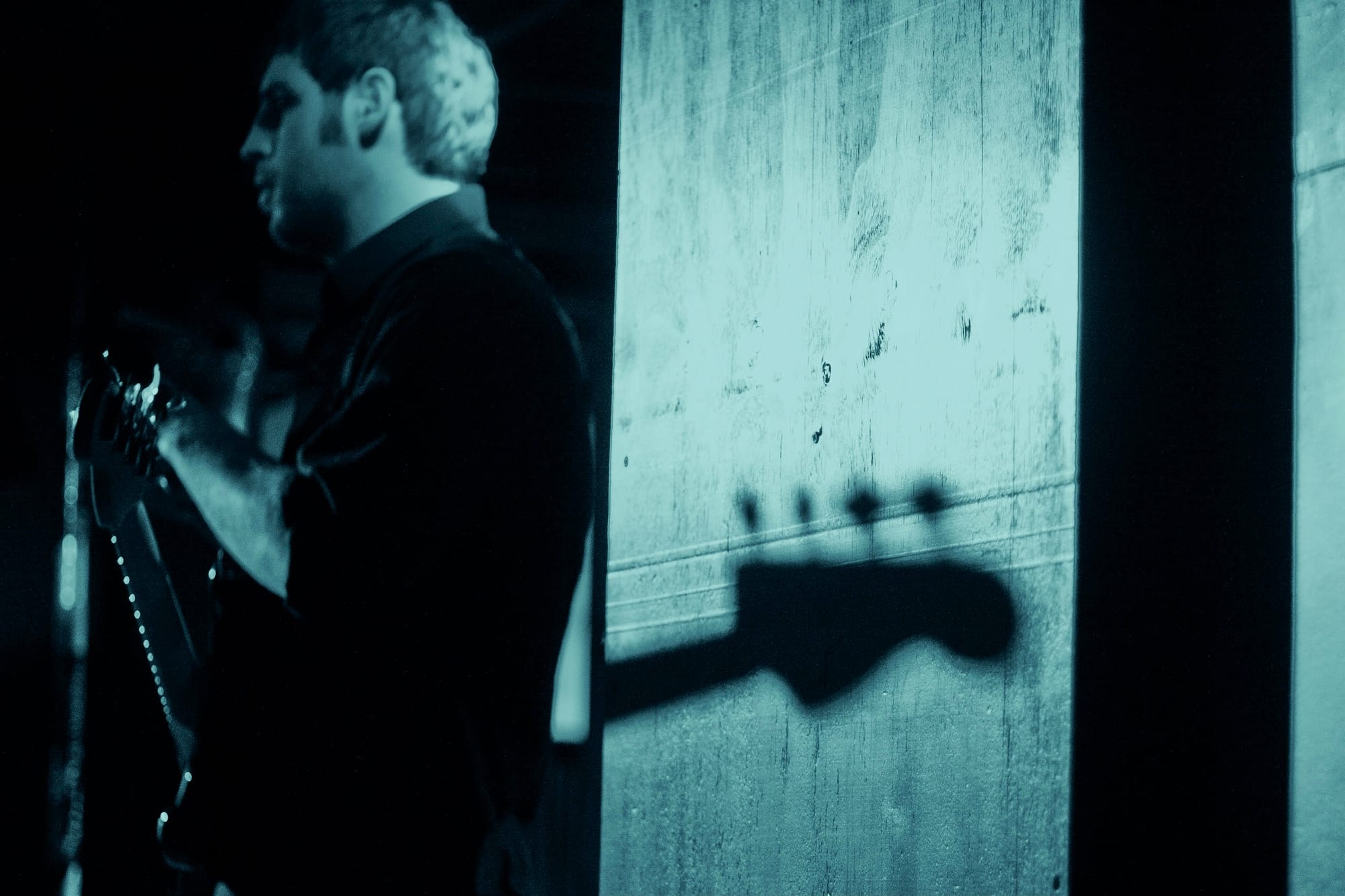 Guitarist crouched low on stage in dramatic rim lighting during a live music performance.