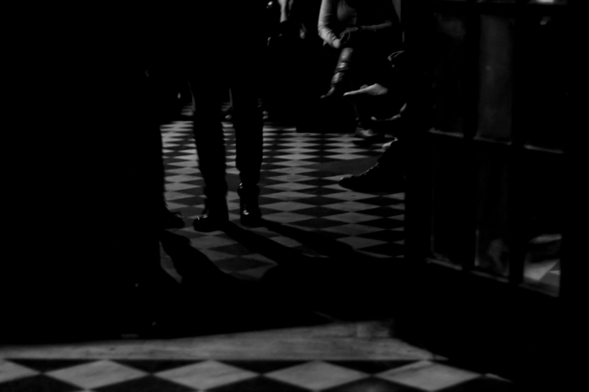 Open French doors looking at patrons on a diamond checkerboard tile floor at a music venue.