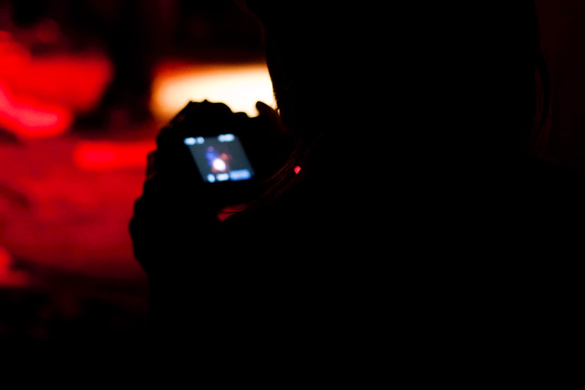 Silhouetted concert attendee holding up a camera with the glowing screen framing the stage.