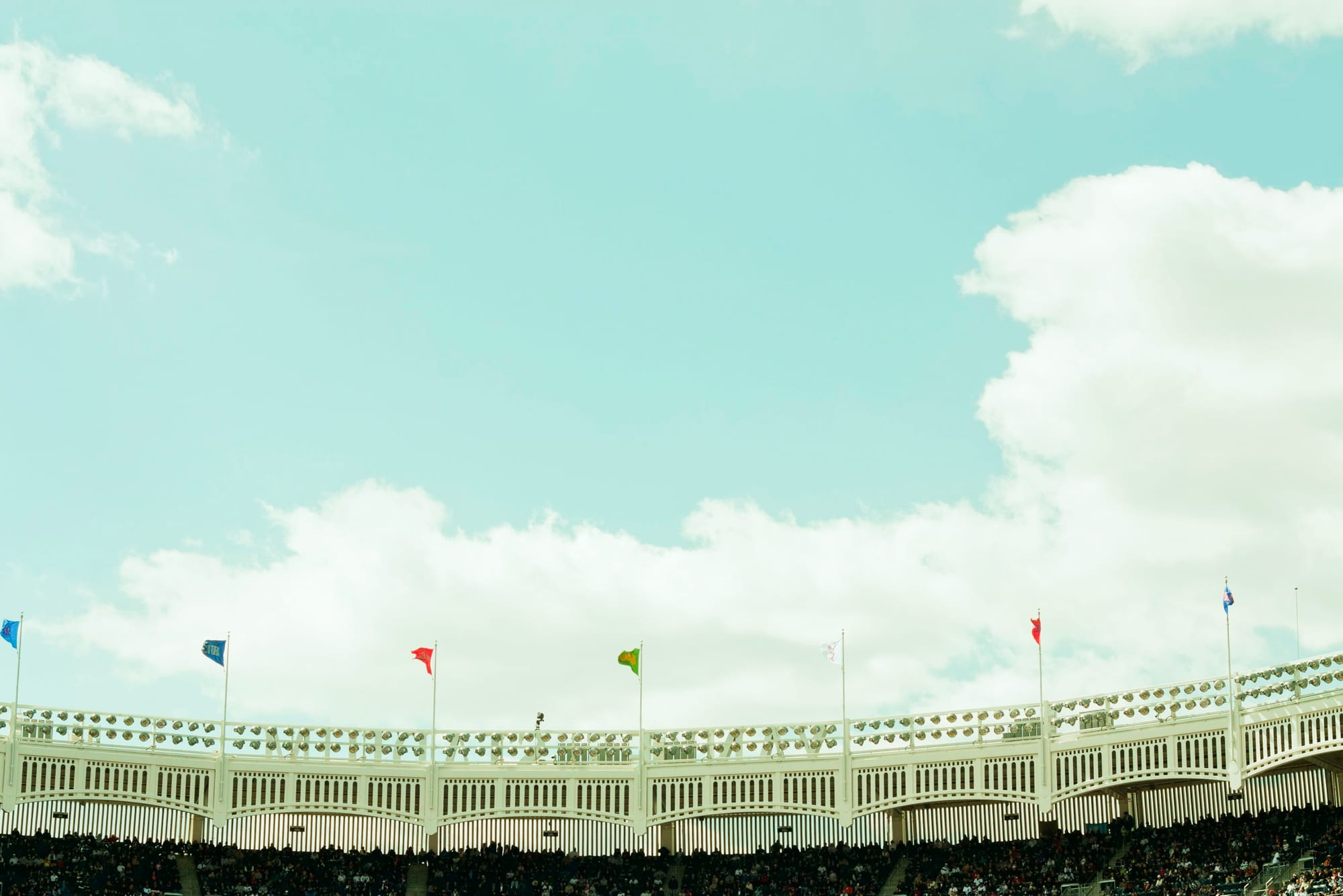 White frieze and floodlights of Yankee Stadium with flags against a blue sky for Tigers vs Yankees.