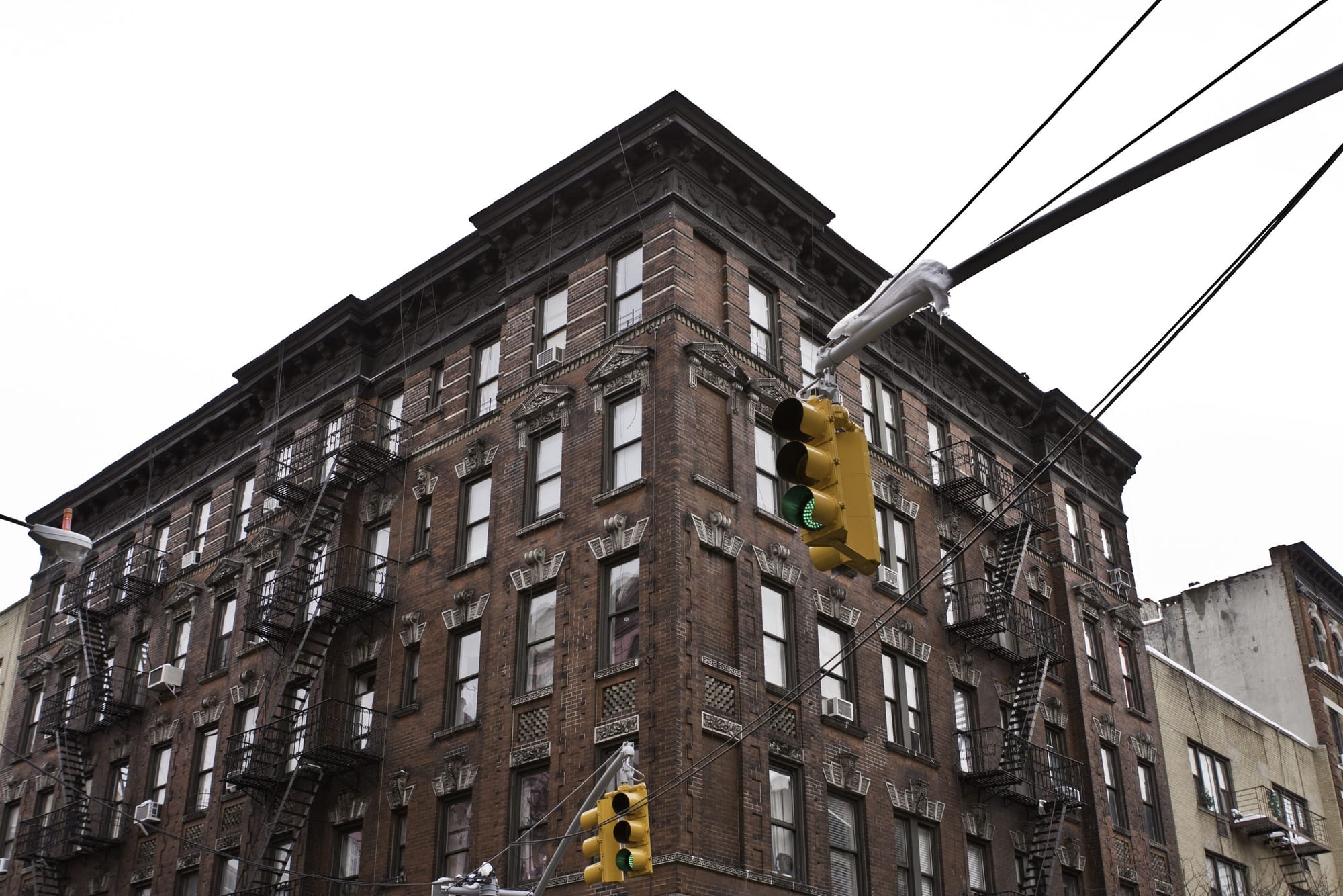 Low-angle view of a classic brick apartment building in Lower Manhattan with yellow traffic signals against an overcast sky.