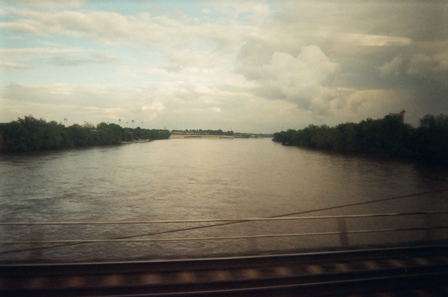 View from a train window looking across a wide brown river bordered by green trees between NYC and DC.