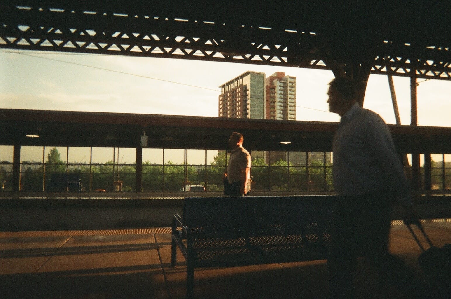 Commuters walking across a sun-drenched train station platform in warm evening light between NYC and DC.