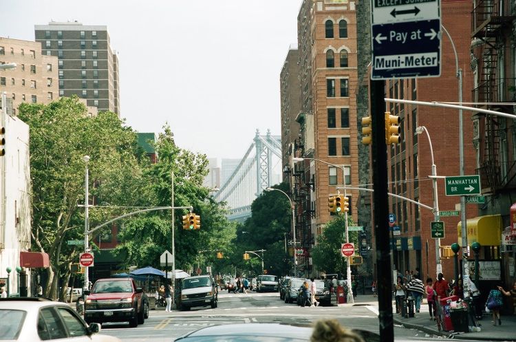 Lower Manhattan's East Broadway framed by tenements and signs pointing toward the Manhattan Bridge.